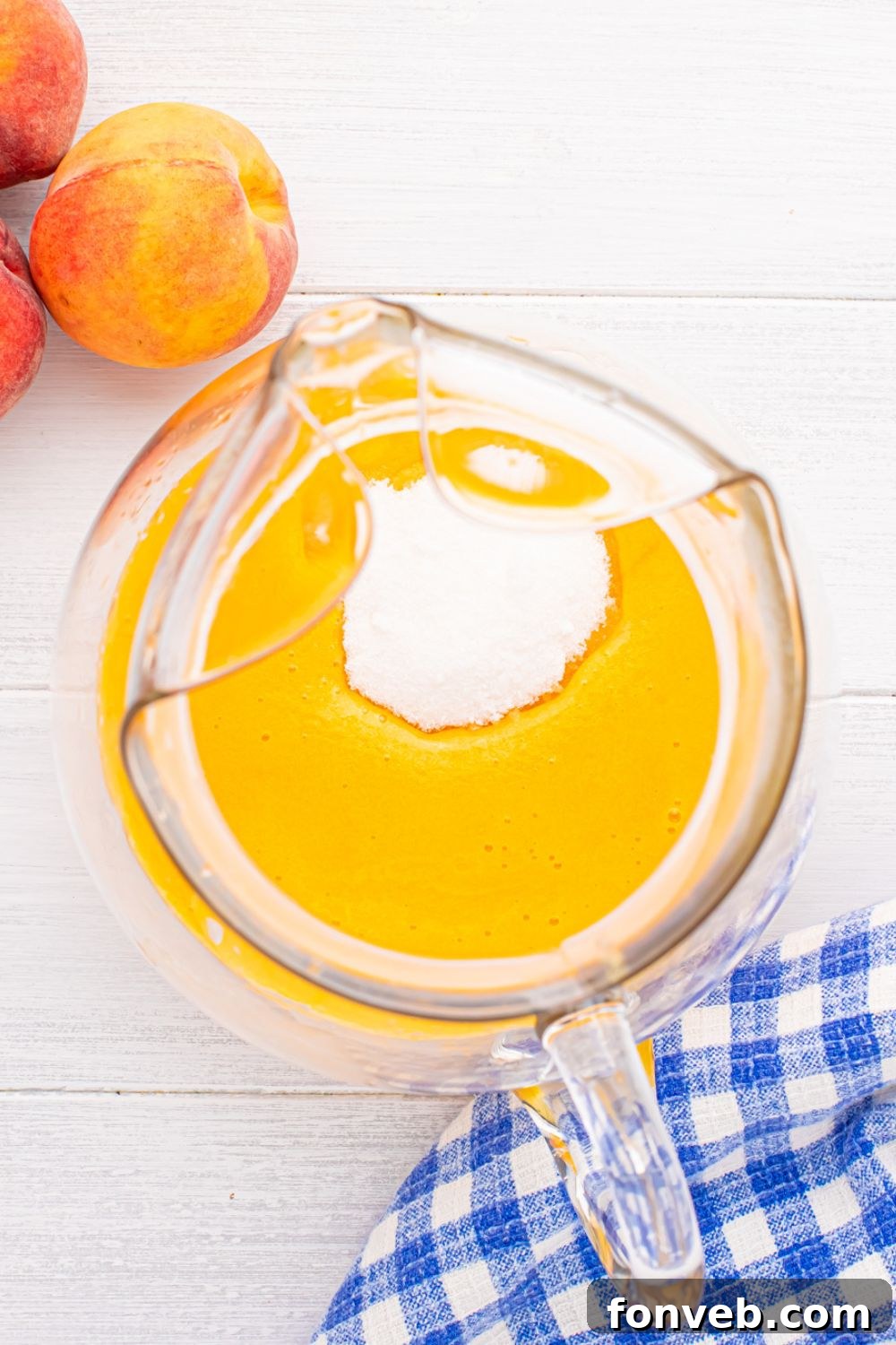 sugar poured into the peach tea mixture in a large pitcher sitting on table 