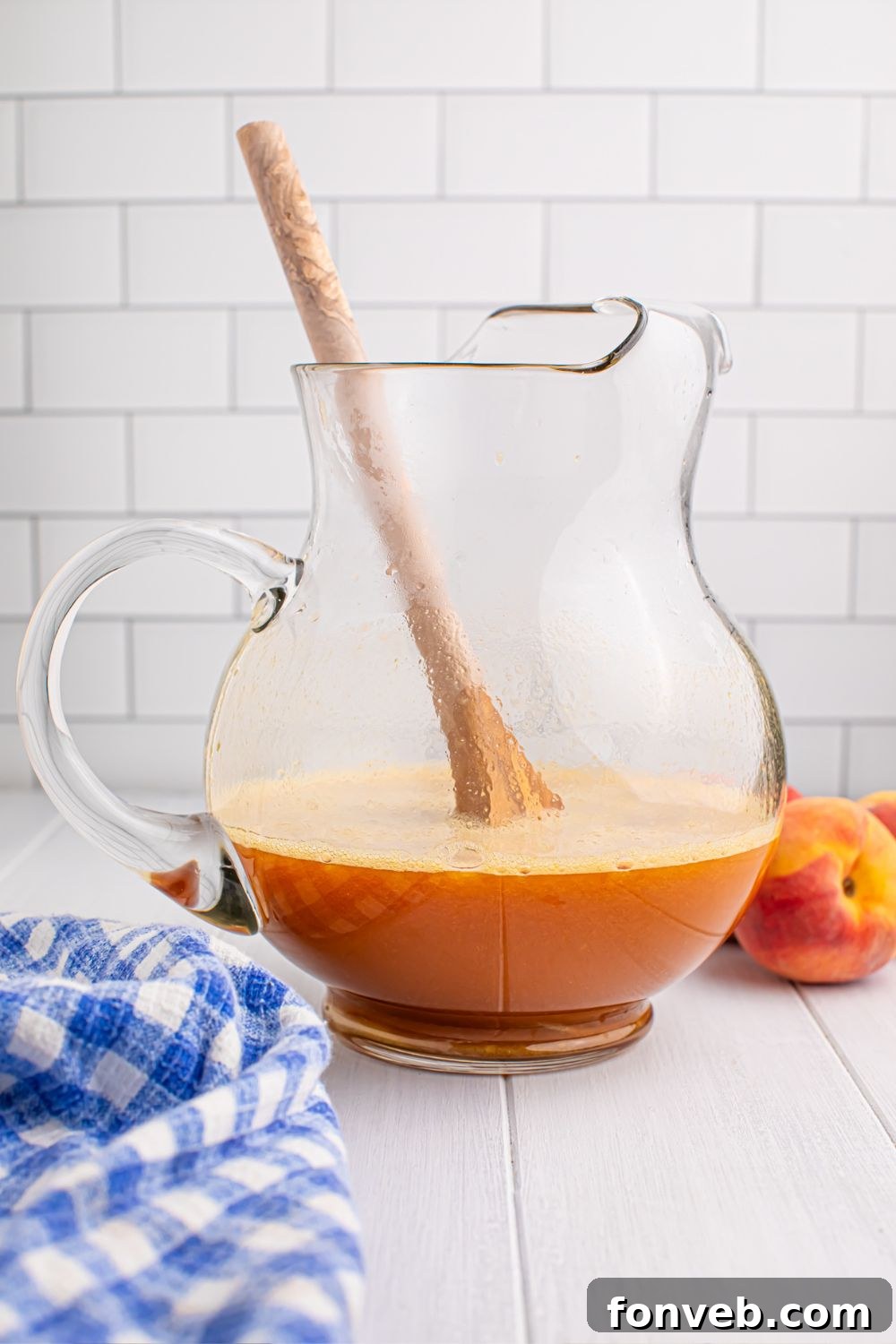 peach blended mixture in a large pitcher being stirred with a wooden spoon 