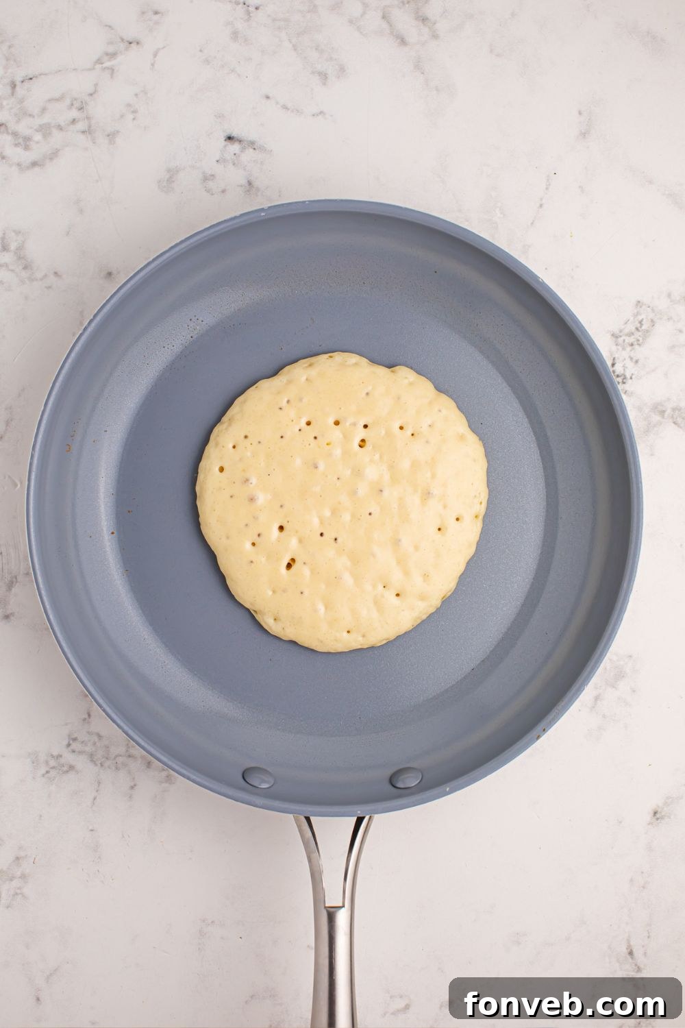 Uncooked pancake batter poured into a hot skillet, just beginning to bubble.