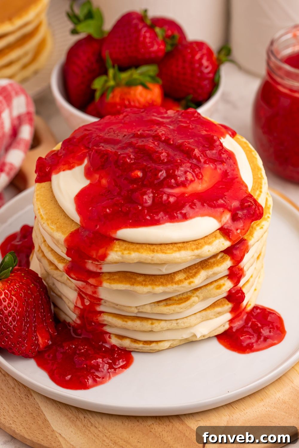 A close-up of a stacked Strawberry Cheesecake Pancake, with generous strawberry sauce dripping down the sides.