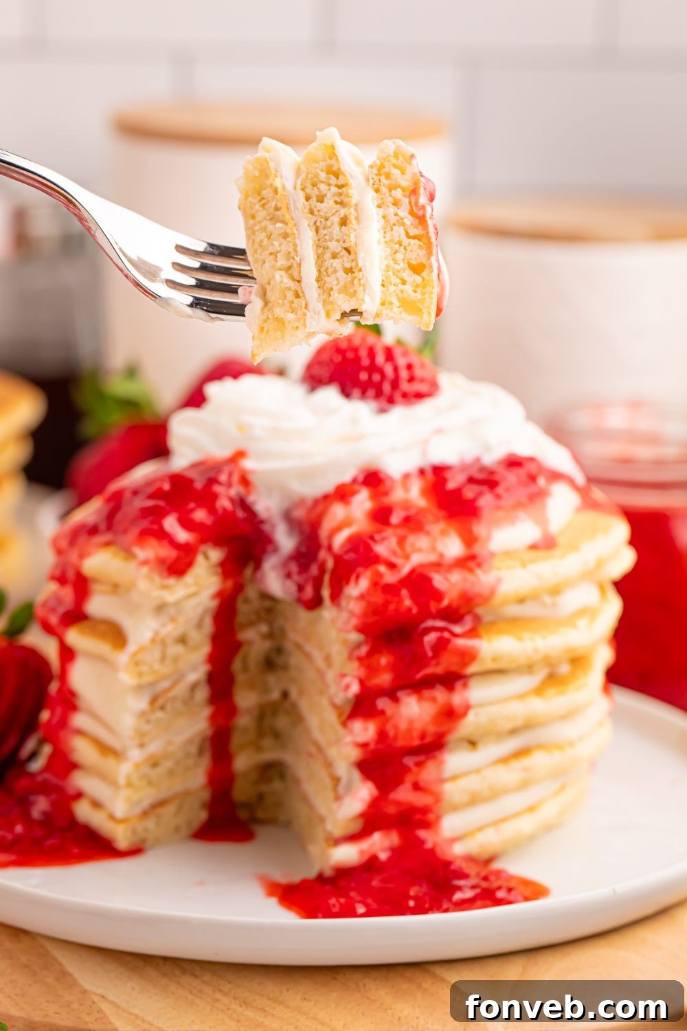 A plate of Strawberry Cheesecake Pancakes with a fork holding a mouthful of pancake, cheesecake, and strawberry sauce.