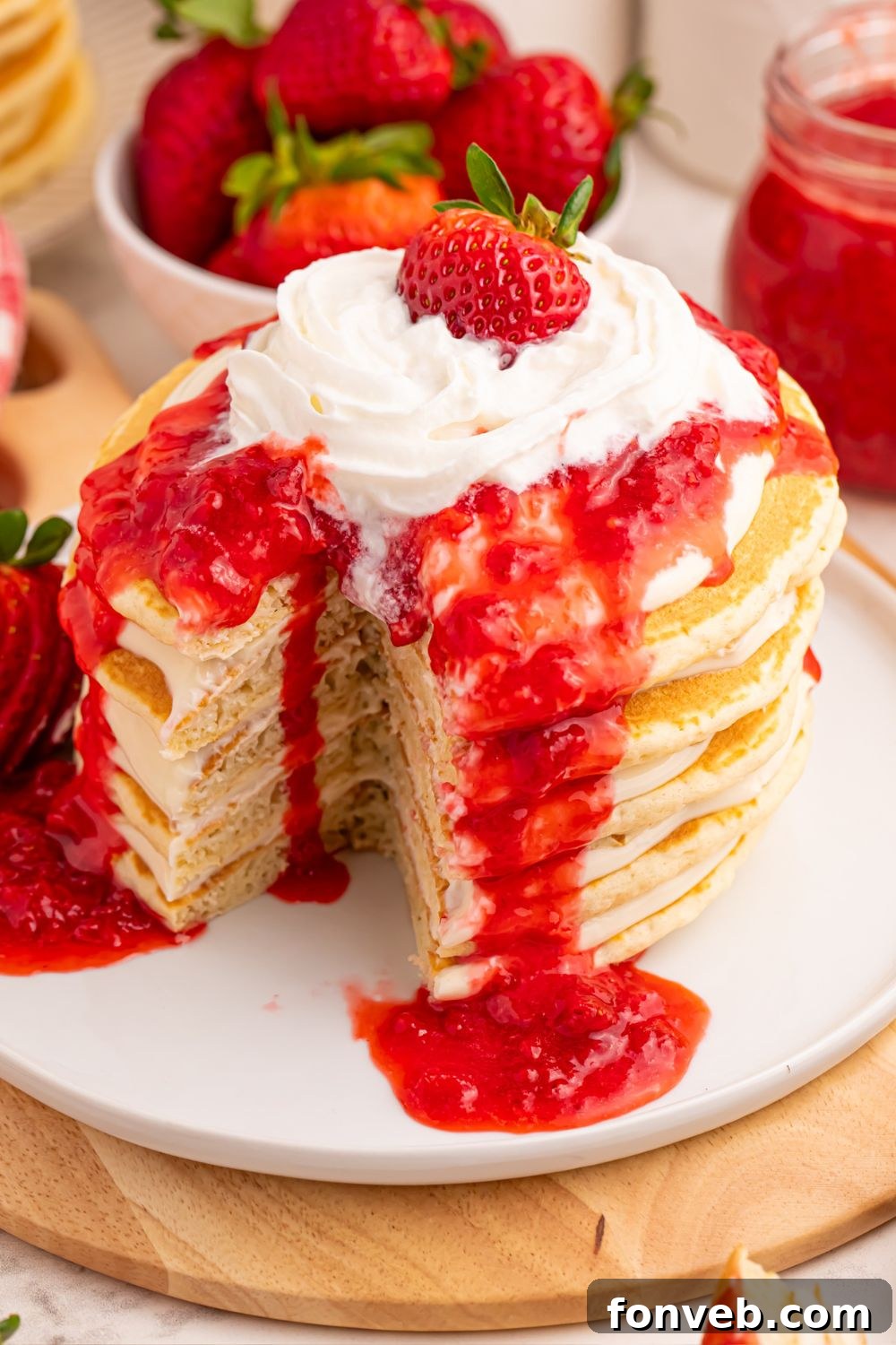 Strawberry Cheesecake Pancakes on a plate, with a portion cut out, showing melting whipped cream on top.