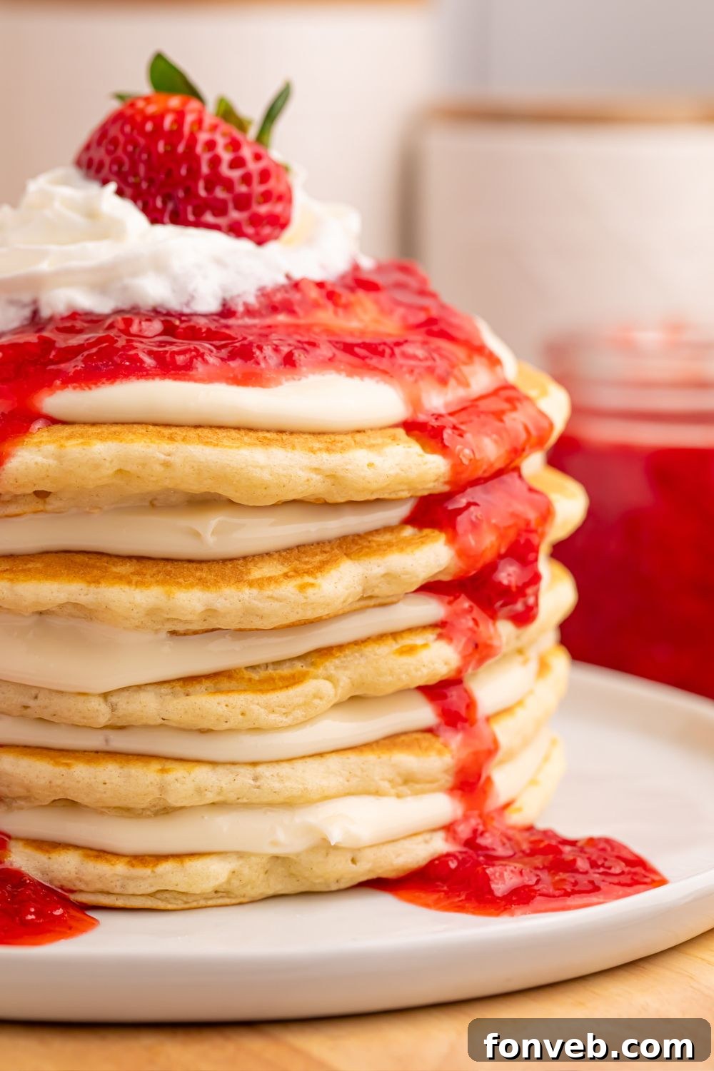 Side view of a Strawberry Cheesecake Pancake with cream cheese spread and fresh strawberries on top, served on a white plate.