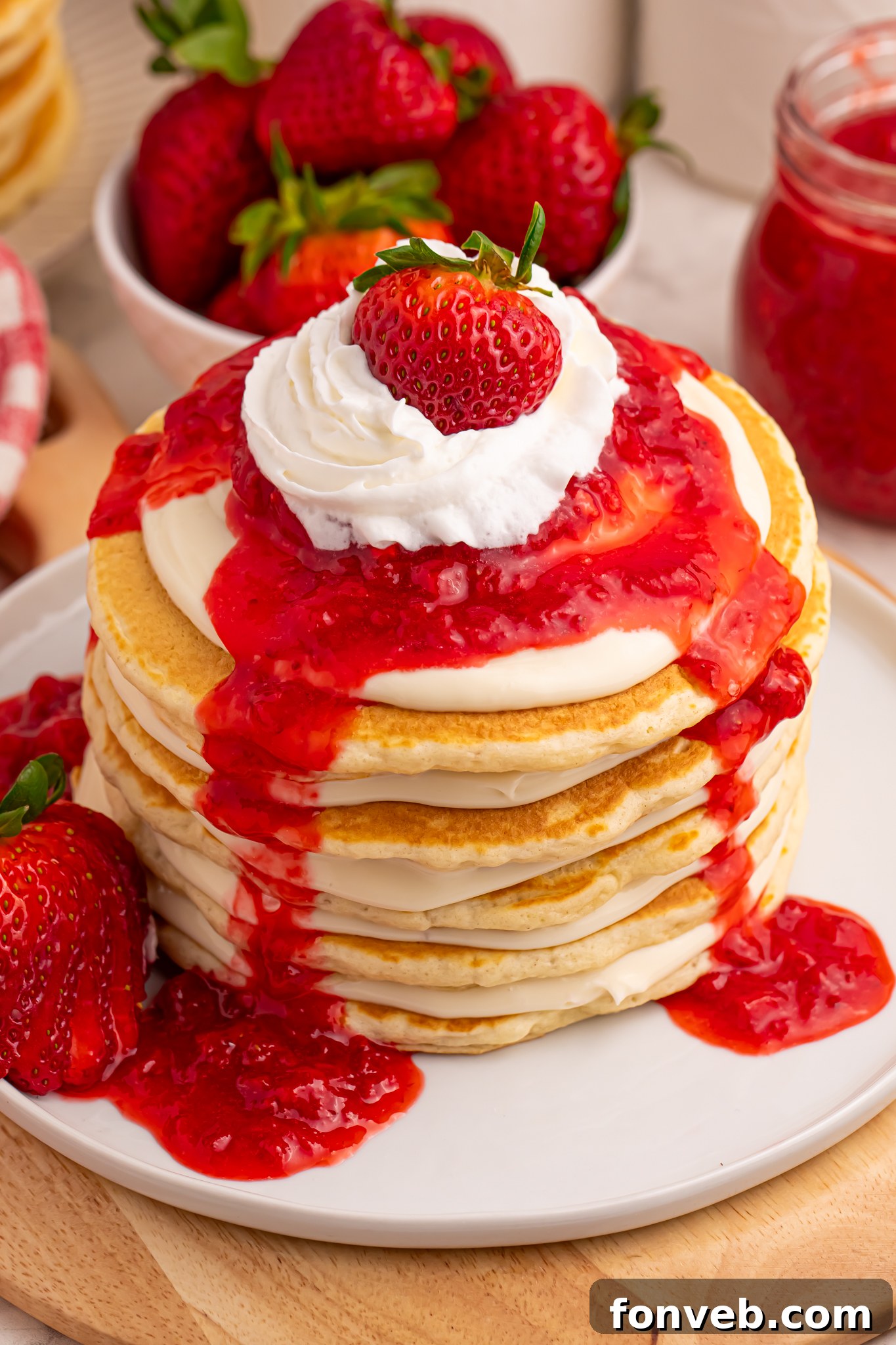 Strawberry Cheesecake Pancakes on a pristine white plate, with luscious strawberry sauce elegantly drizzled over the stack.