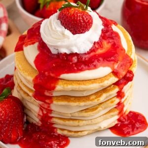 Strawberry Cheesecake Pancakes stacked on a plate with whipped cream and a whole berry on top