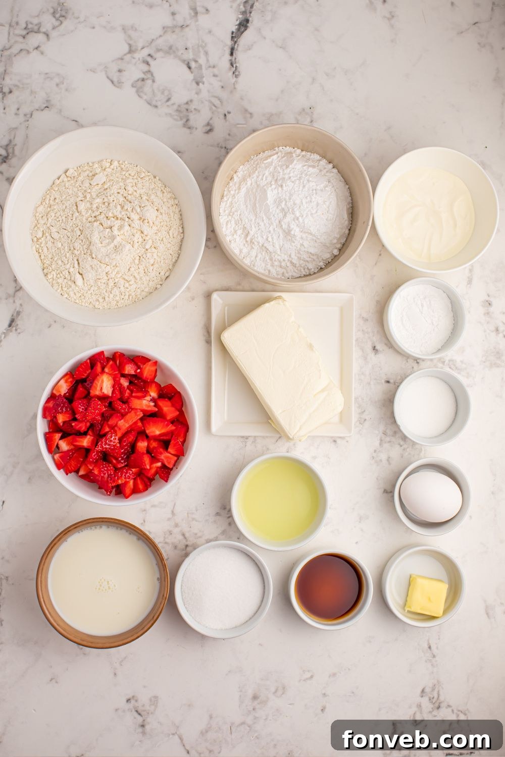 Assorted ingredients for Strawberry Cheesecake Pancakes laid out in individual bowls on a marble countertop.