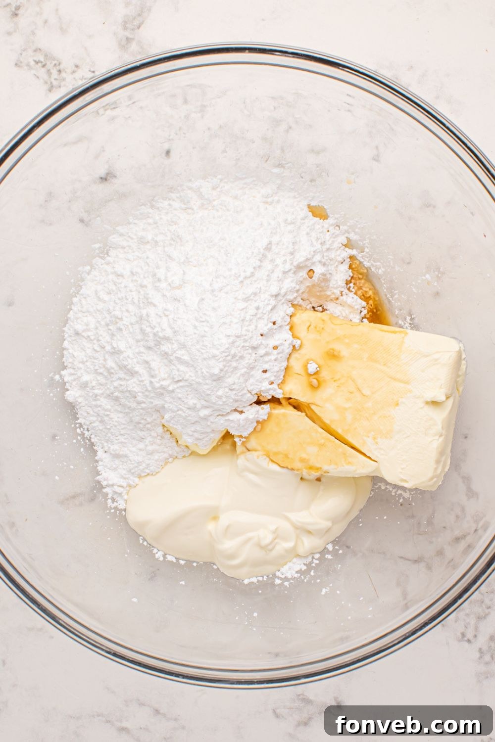 Creamy cheesecake mixture for strawberry cheesecake pancakes prepared in a clear glass bowl on a marble counter.