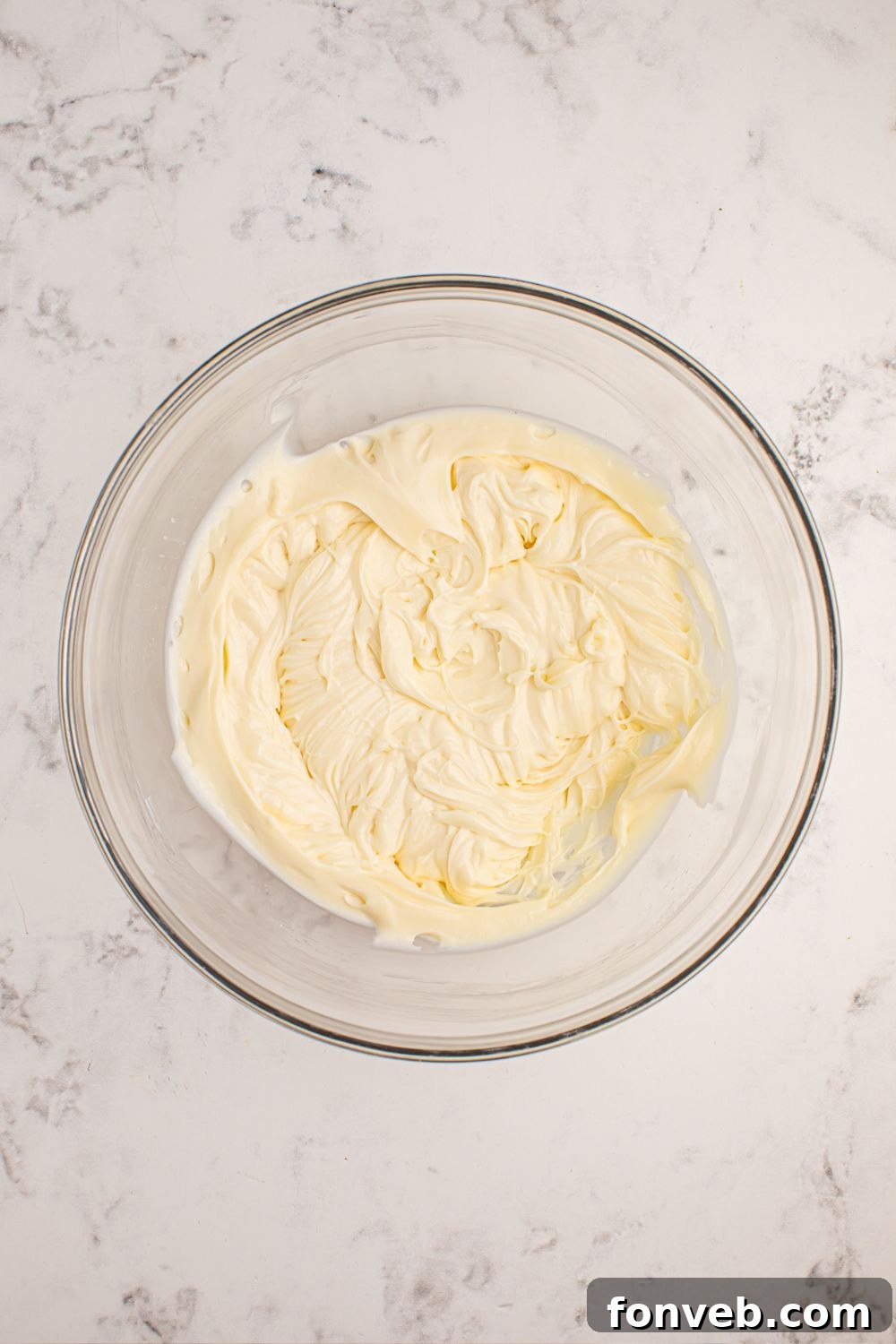 Freshly mixed cheesecake batter in a glass bowl, ready for spreading.