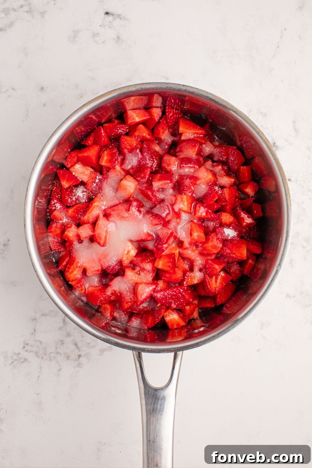 Diced strawberries and sugar resting in a pan, prepped for cooking the strawberry sauce.
