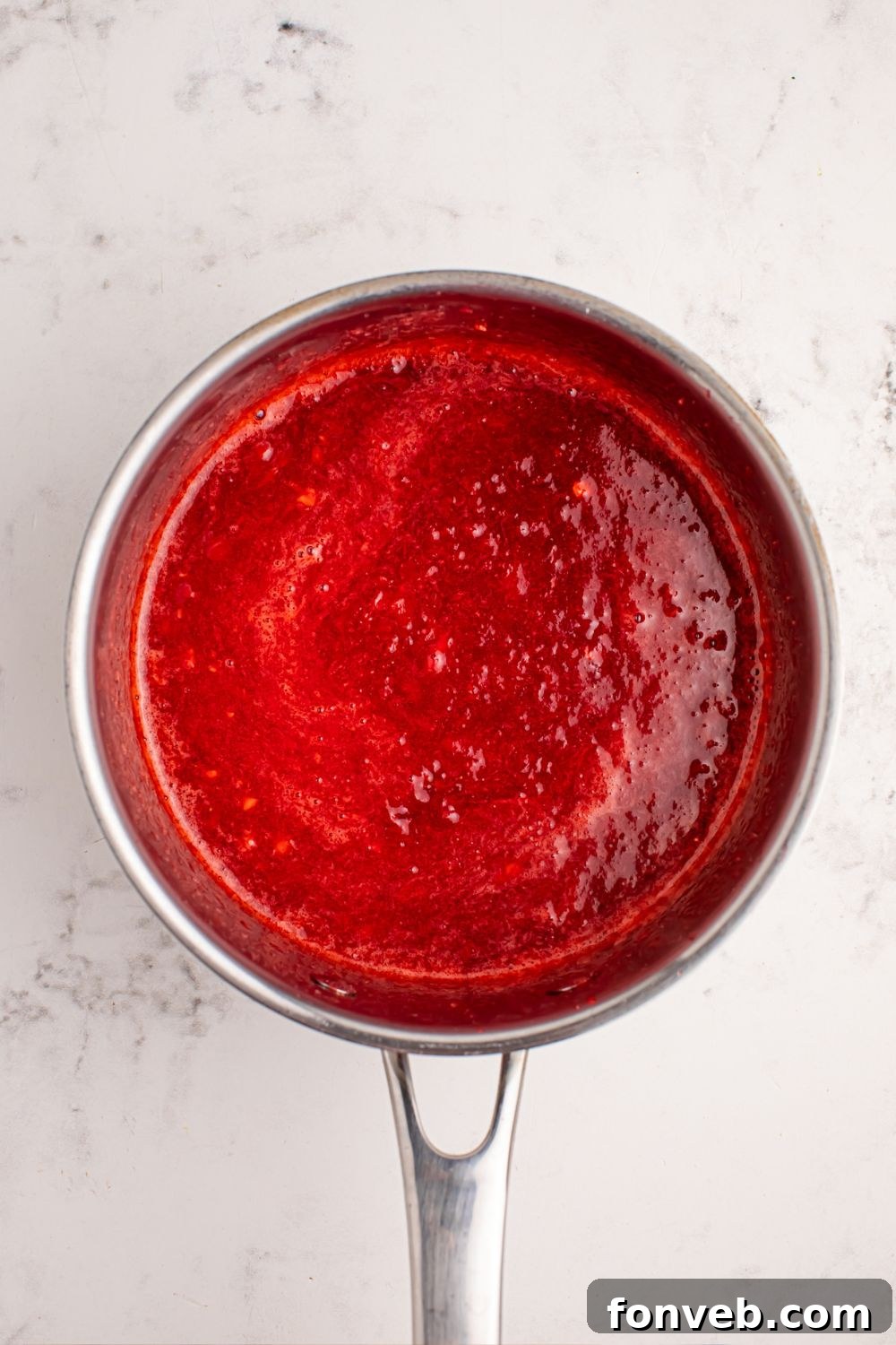Luscious strawberry sauce simmering in a saucepan on the kitchen counter.