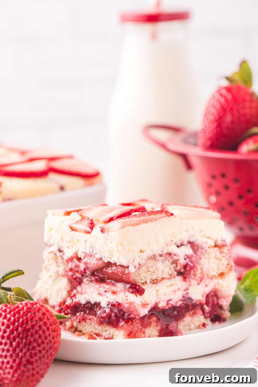 Strawberry Tiramisu sliced and placed on a plate with berries, and a glass of milk behind the plate 