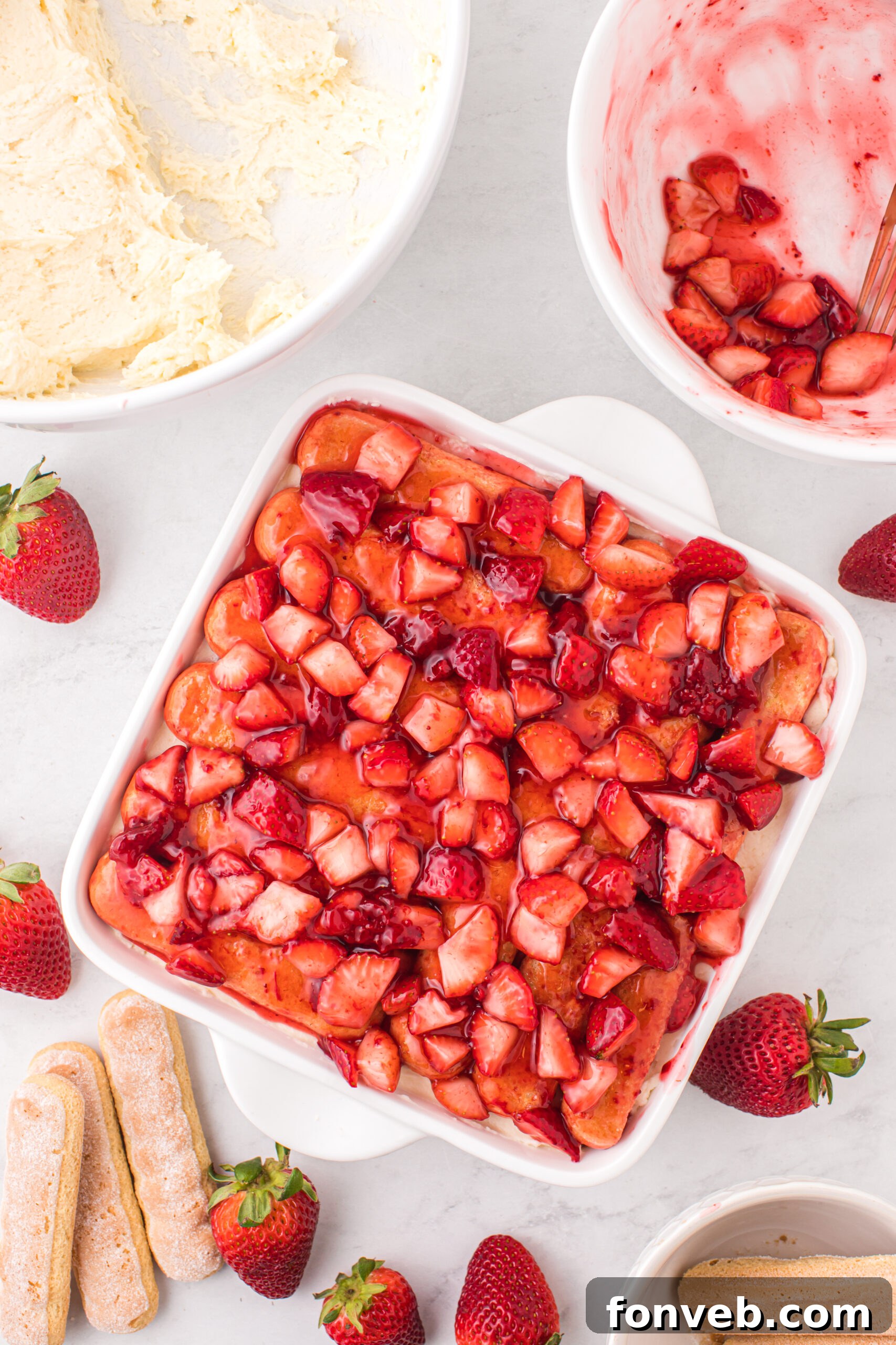 Strawberry Tiramisu on table with a bowl of mascarpone filling and a bowl of strawberries 
