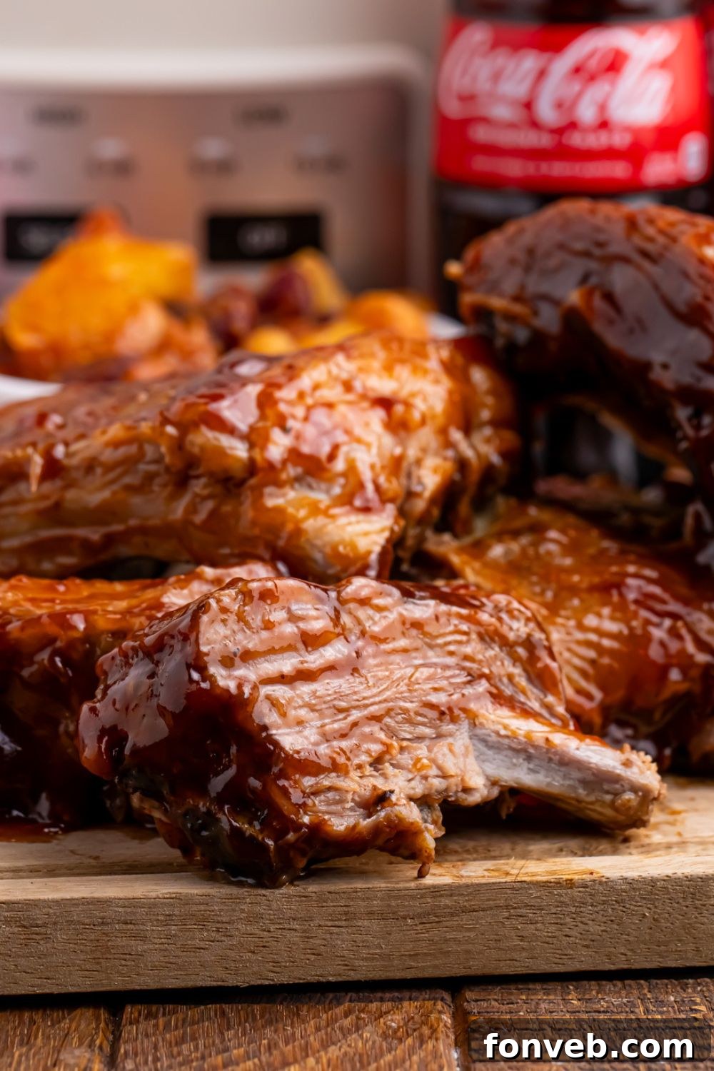 Cooked Slow Cooker Coca Cola Ribs neatly stacked on a cutting board, with the slow cooker in the background