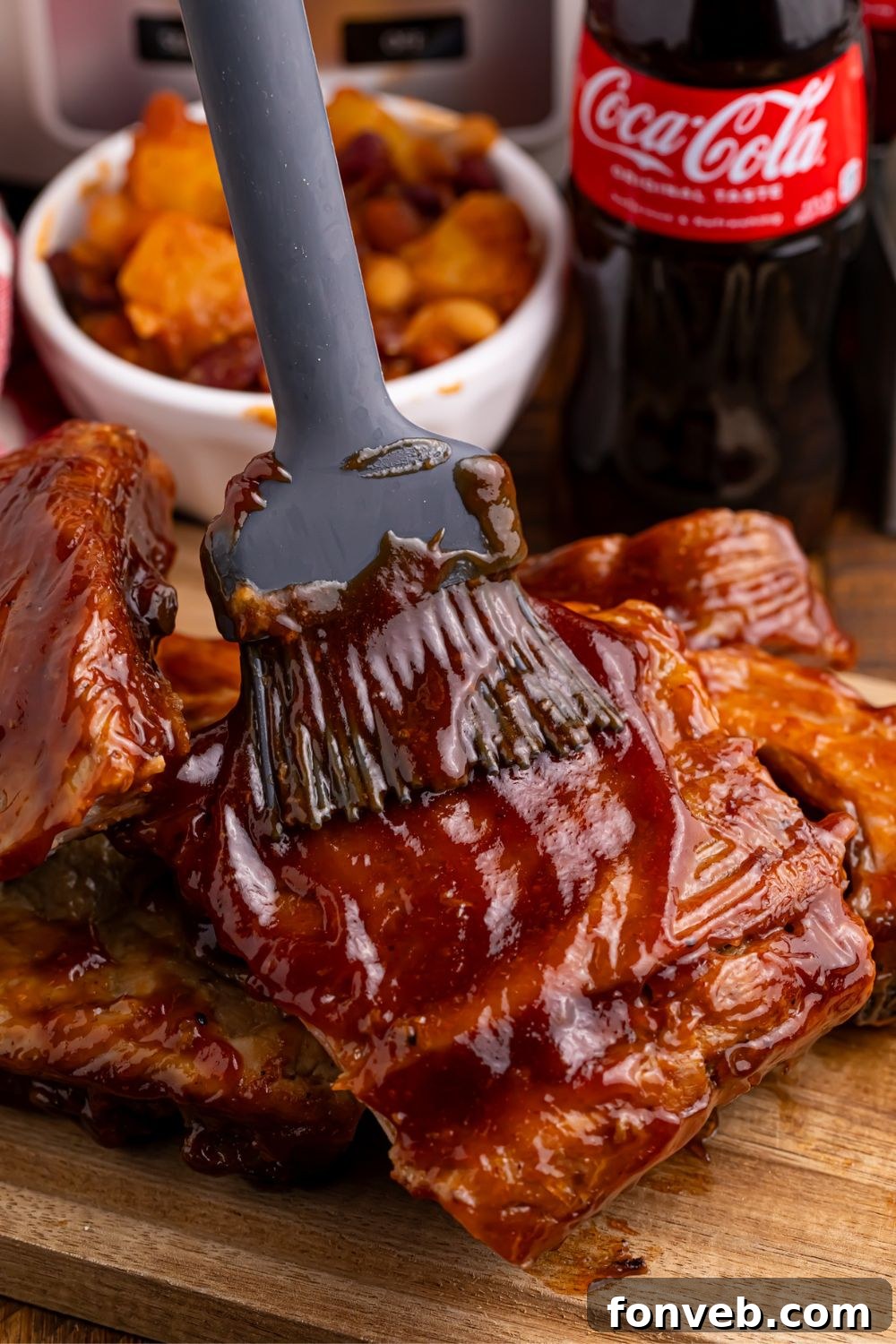 Someone basting Slow Cooker Coca Cola Ribs with extra sauce on a wooden cutting board