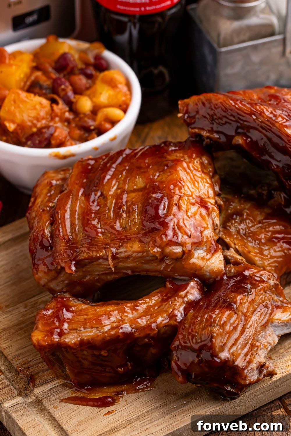 A close-up view of perfectly glazed Slow Cooker Coca Cola Ribs, stacked on a wooden board