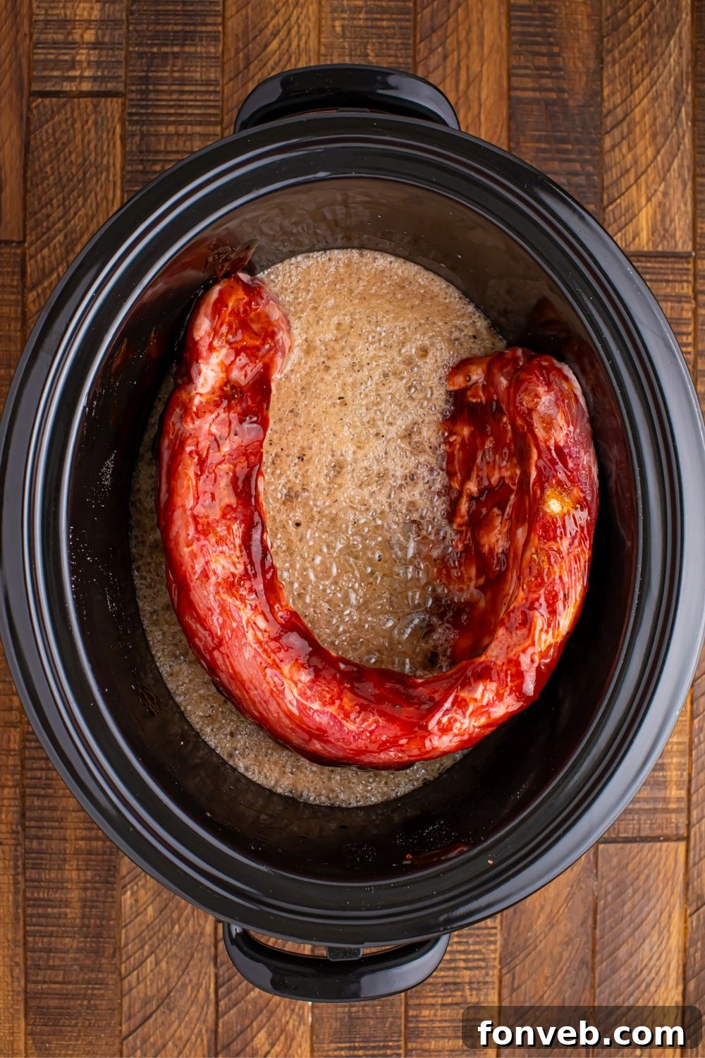 Coca Cola being poured over the ribs in the slow cooker, creating effervescent bubbles