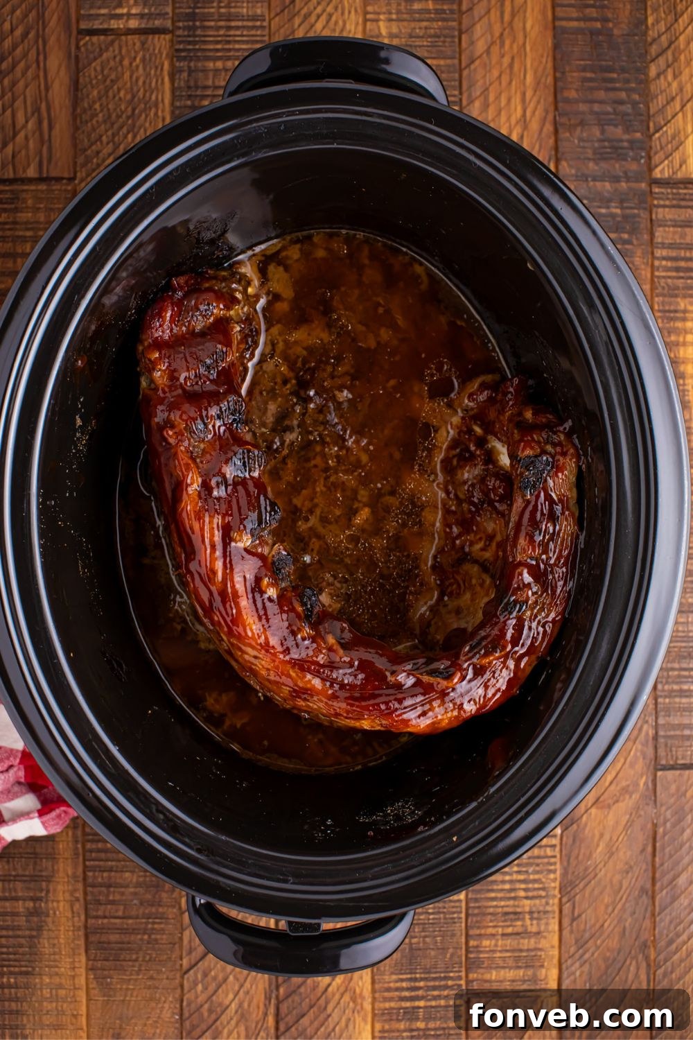 Overhead view of slow cooker with fully cooked Coca Cola Ribs, glistening with sauce