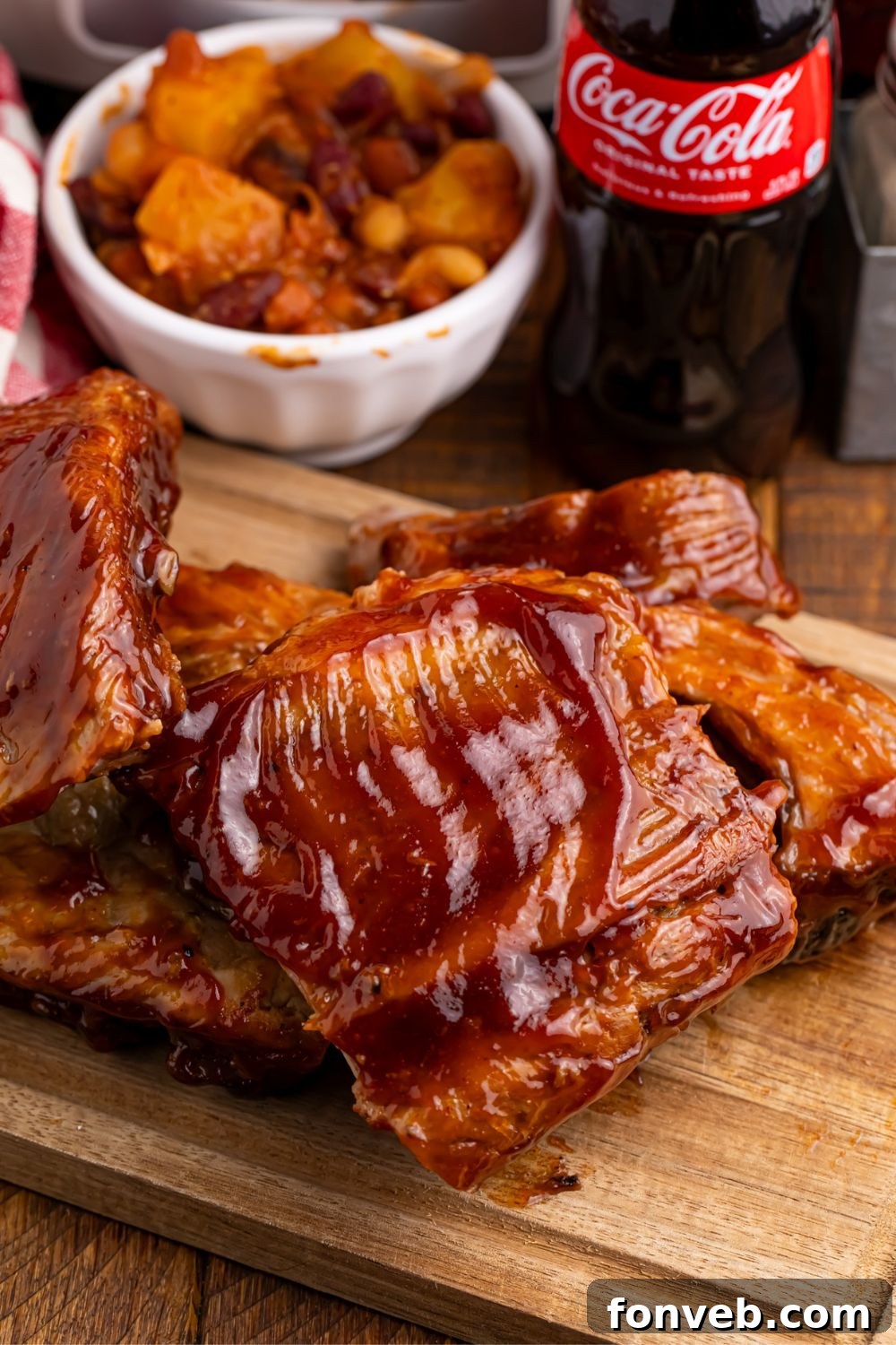 Pork ribs generously smothered in BBQ sauce, stacked enticingly on a wooden cutting board
