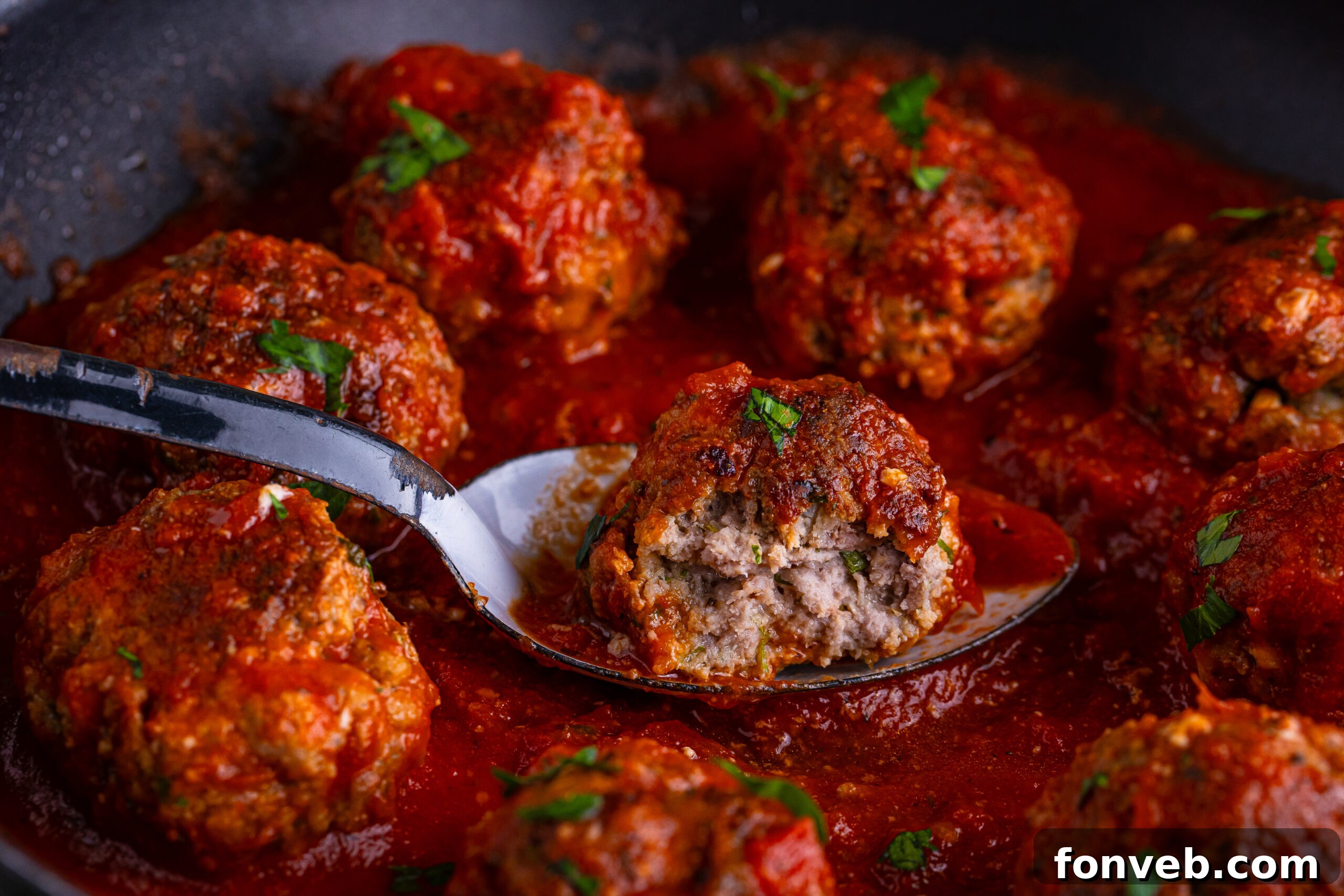 Classic Italian Meatball with a bite taken out of it close up in a pan with a marinara sauce drizzled on top 
