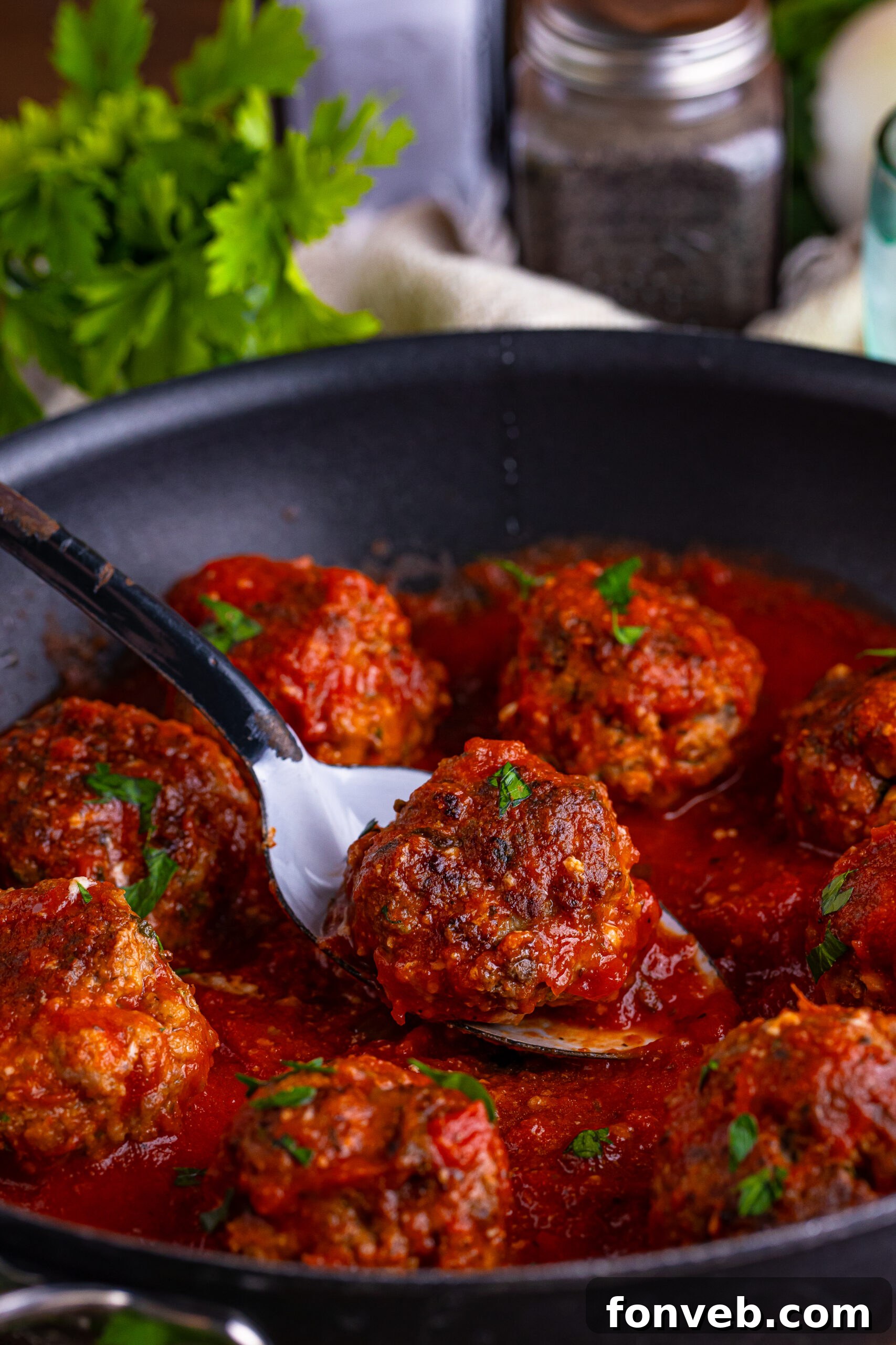 italian meatballs in a skillet with a spoon lifting one up 
