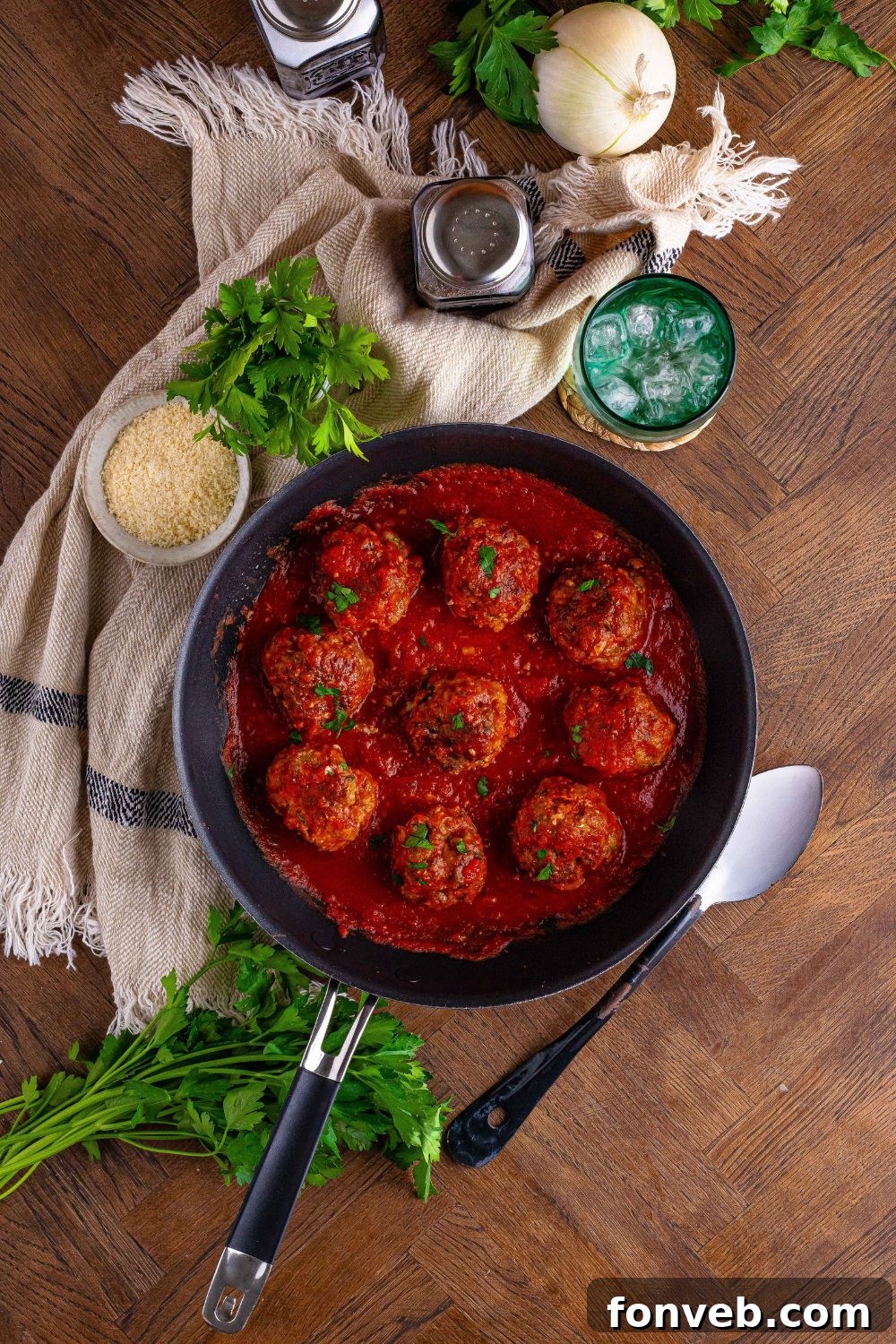 Classic Italian Meatballs in a skillet with garnishes around the pan 