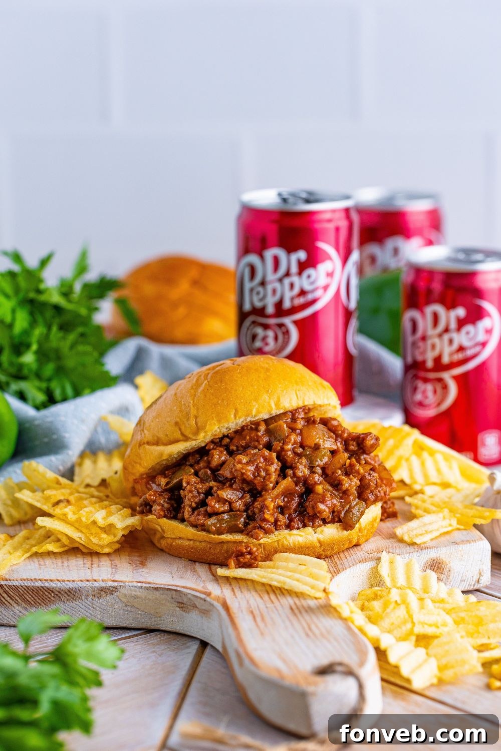 Dr. Pepper Sloppy Joes on a cutting board with chips and cans of pop around it 
