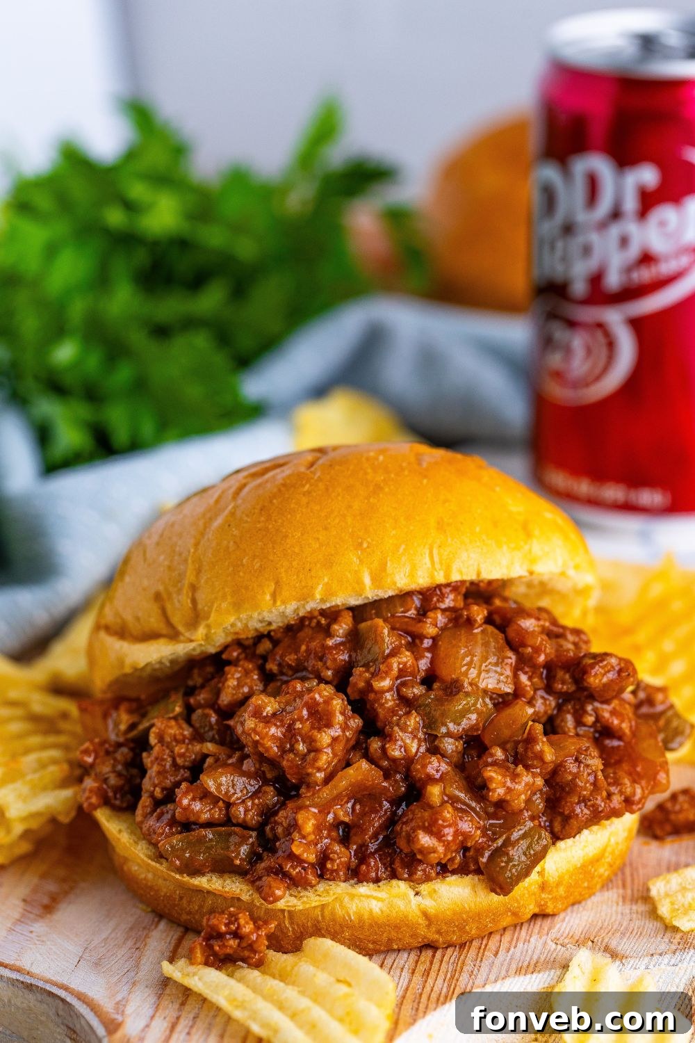 hamburger bun loaded with Dr. Pepper sloppy joe mix with a few ruffled chips around it