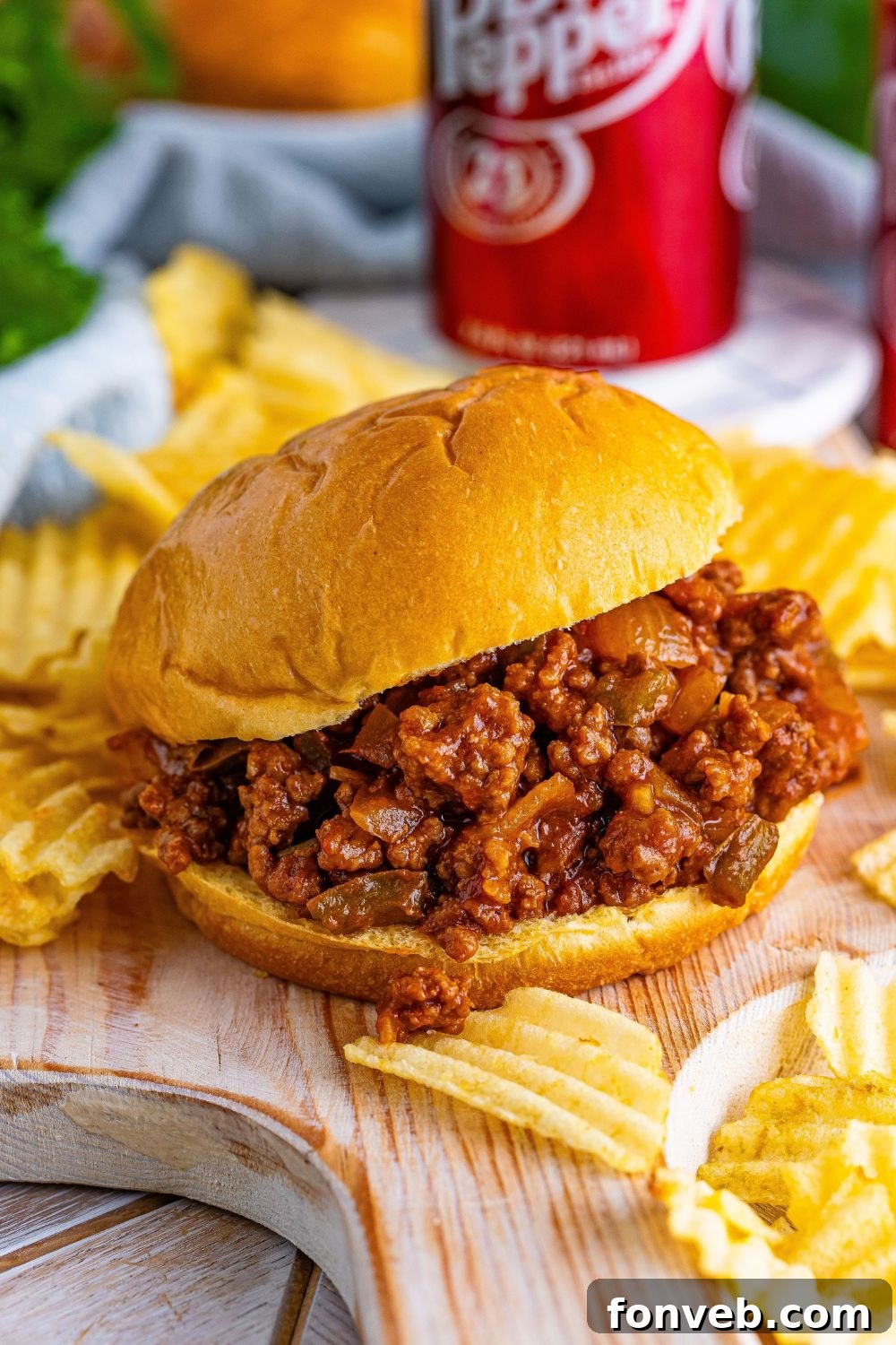 Dr. Pepper Sloppy Joes on table with plain chips spread around the bun and then a few cans of pop in background 