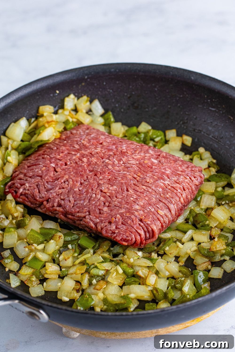 Dr. Pepper Sloppy Joes being cooked with sauted onions and peppers wih ground beef on top 