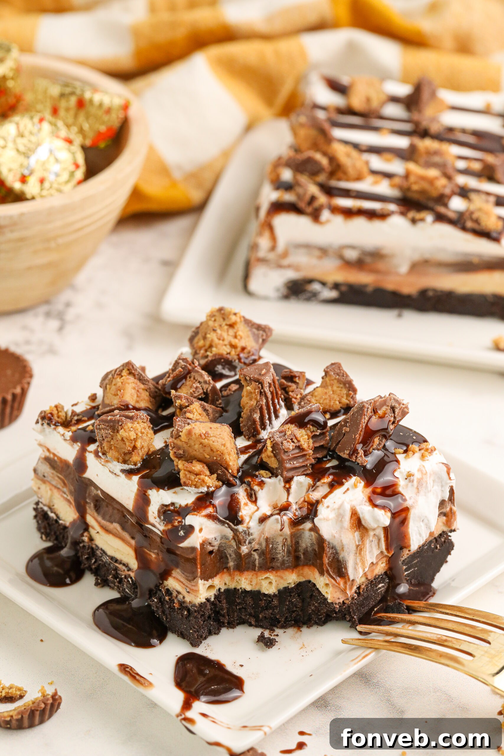 Peanut Butter Chocolate Sweet Stack 2 Reeses Lasagna on a white plate with one bite taken out of it topped with crumbled reeses cups