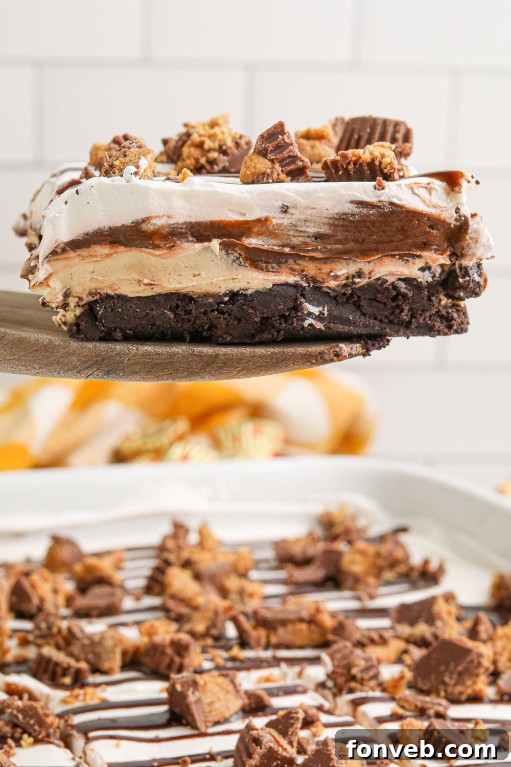 Peanut Butter Chocolate Sweet Stack 13 Reeses Lasagna in a pan with one slice being lifted out of pan with a spatula