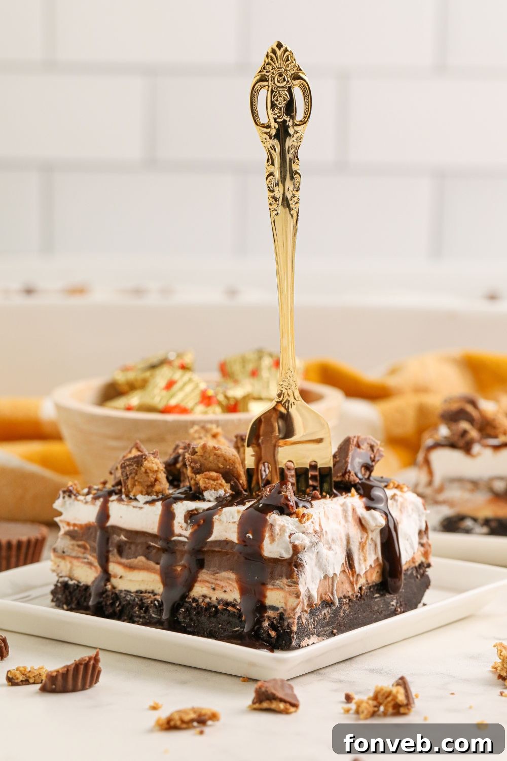 Peanut Butter Chocolate Sweet Stack 4 Reeses Lasagna slice on table with a fork in it and a bowl of Reese's behind it