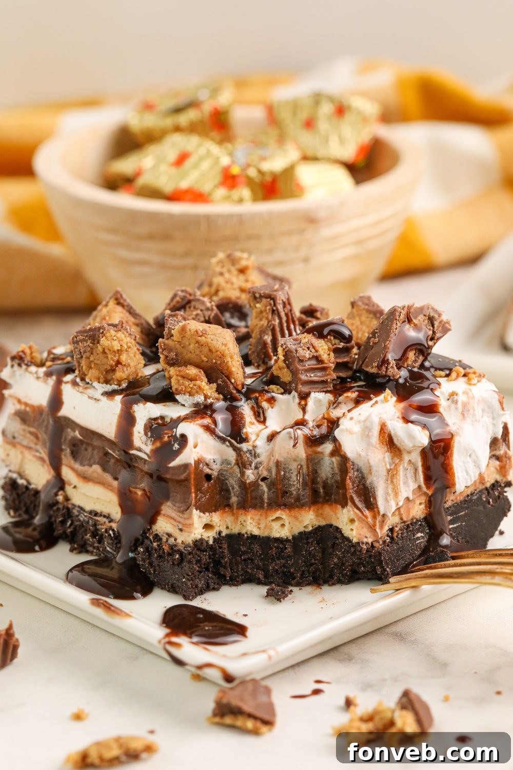 Peanut Butter Chocolate Sweet Stack 5 Reeses Lasagna on a plate with a bite taken out and a bowl of mini reese's in the background with wrappers on them