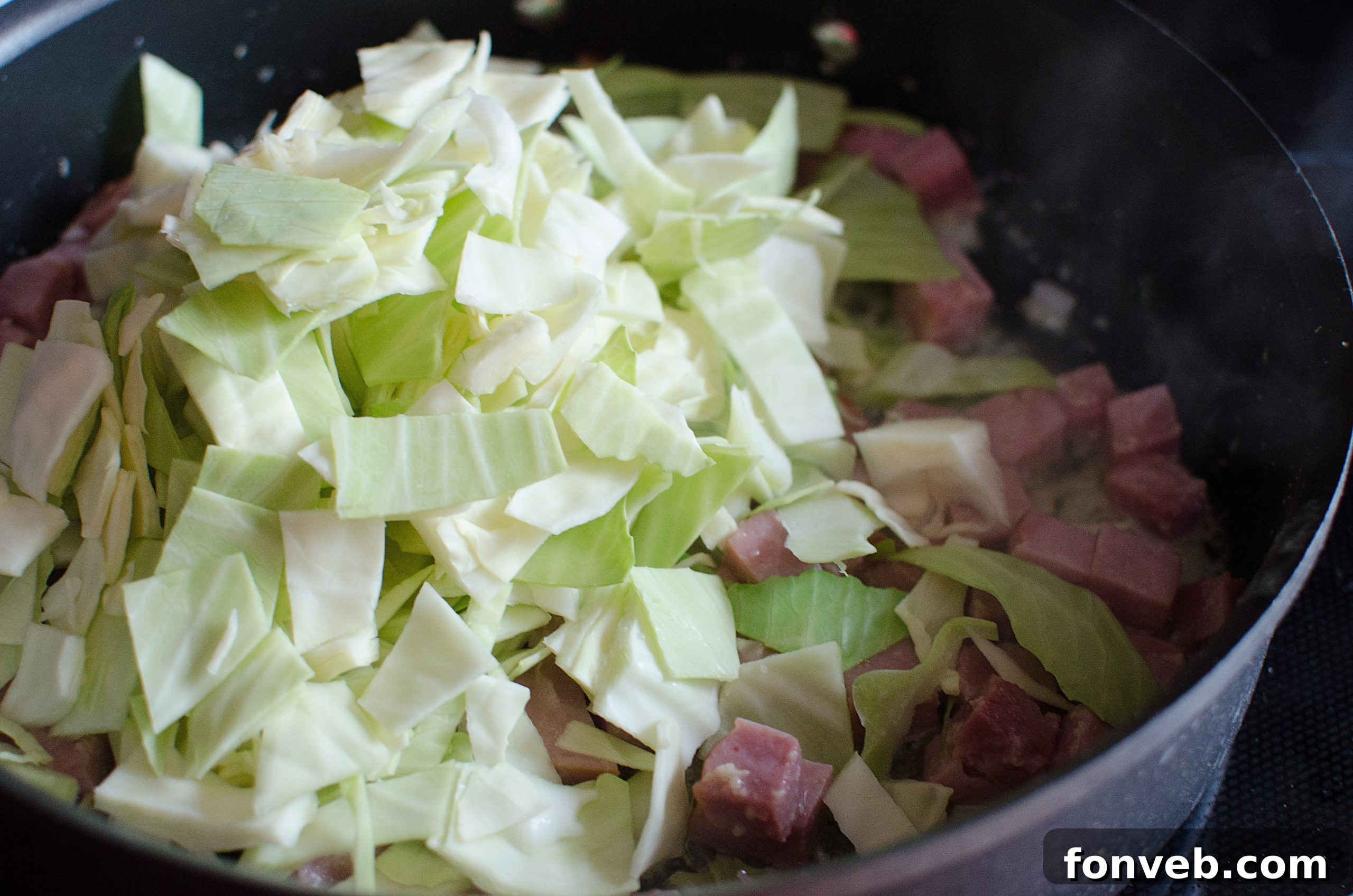 A large skillet filled with sautéing cabbage and onions, releasing aromatic steam.