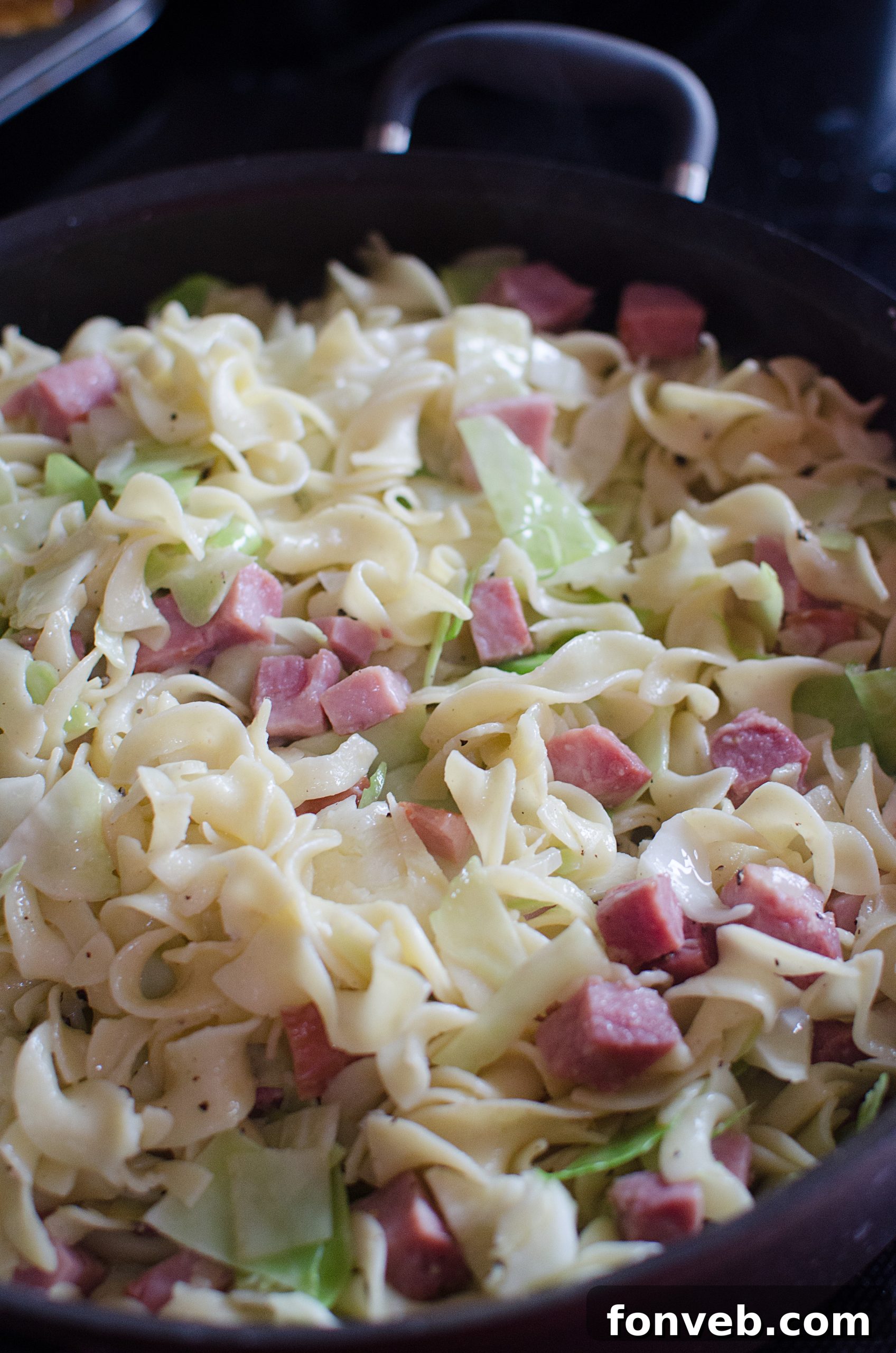 Cooked egg noodles being drained in a colander, ready to be added to the cabbage and ham.