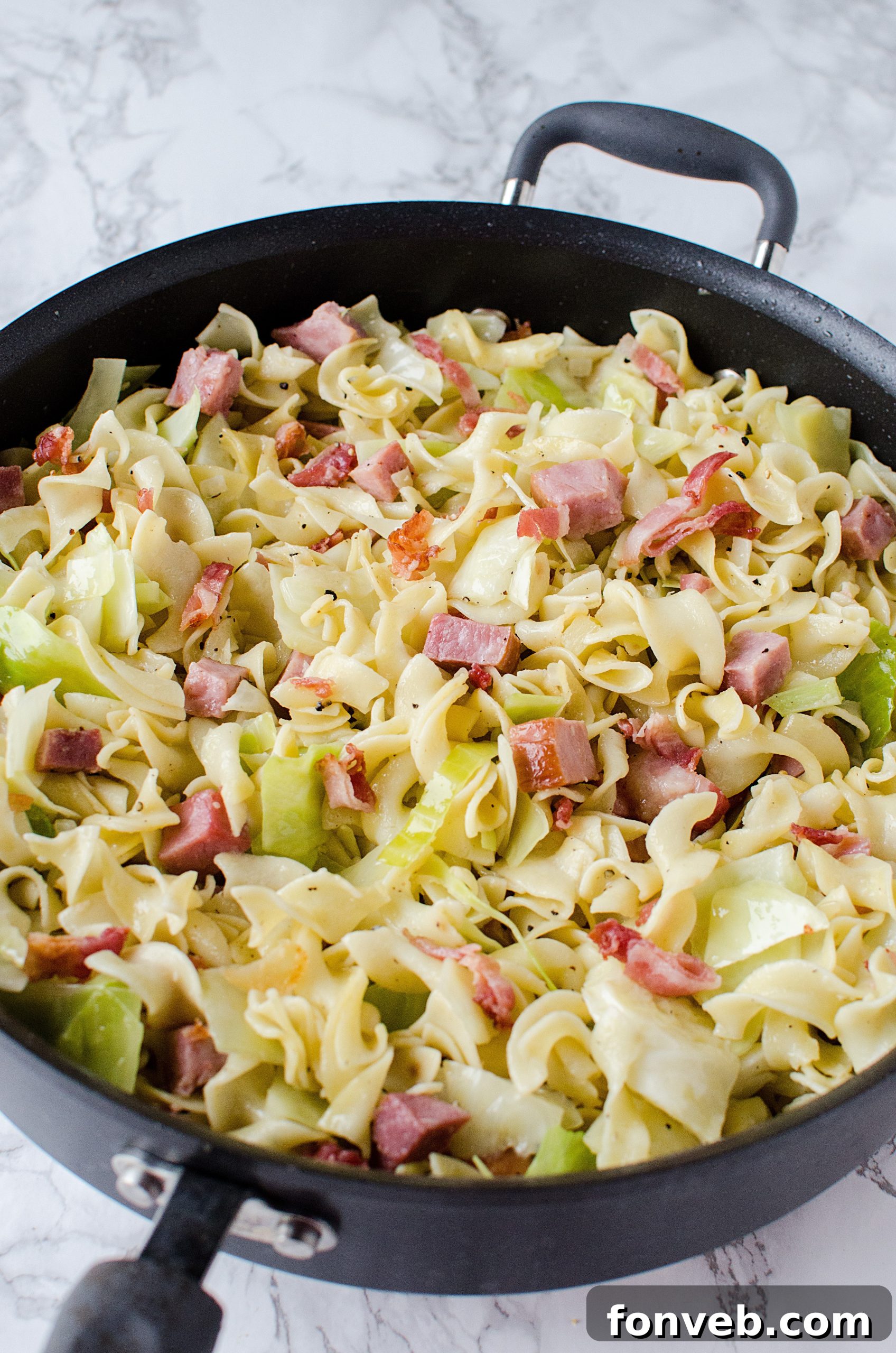 The cooking process of Haluski, with cabbage, ham, and noodles combined in a large skillet.