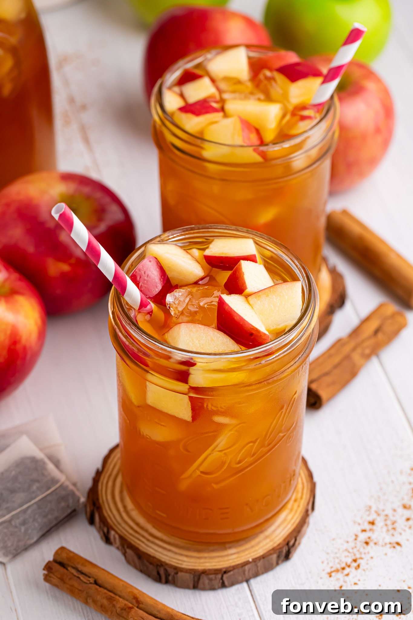 apple cider iced tea in a glass with a shot of the glass with a straw in it and diced fresh apples with ice cubes