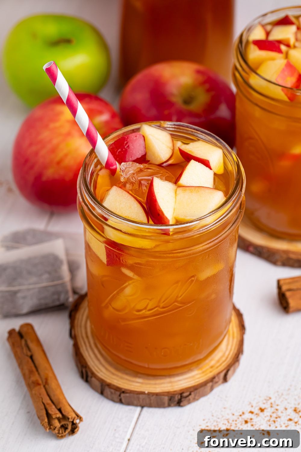 iced tea ciders in glasses with a cinnamon stick, tea bags, and apples on table around the glasses to show what flavors you will taste in the drink