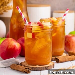 Apple Cider Iced Tea glasses on table with apples and cinnamon sticks around glasses and a red and white striped straw in each mason glass