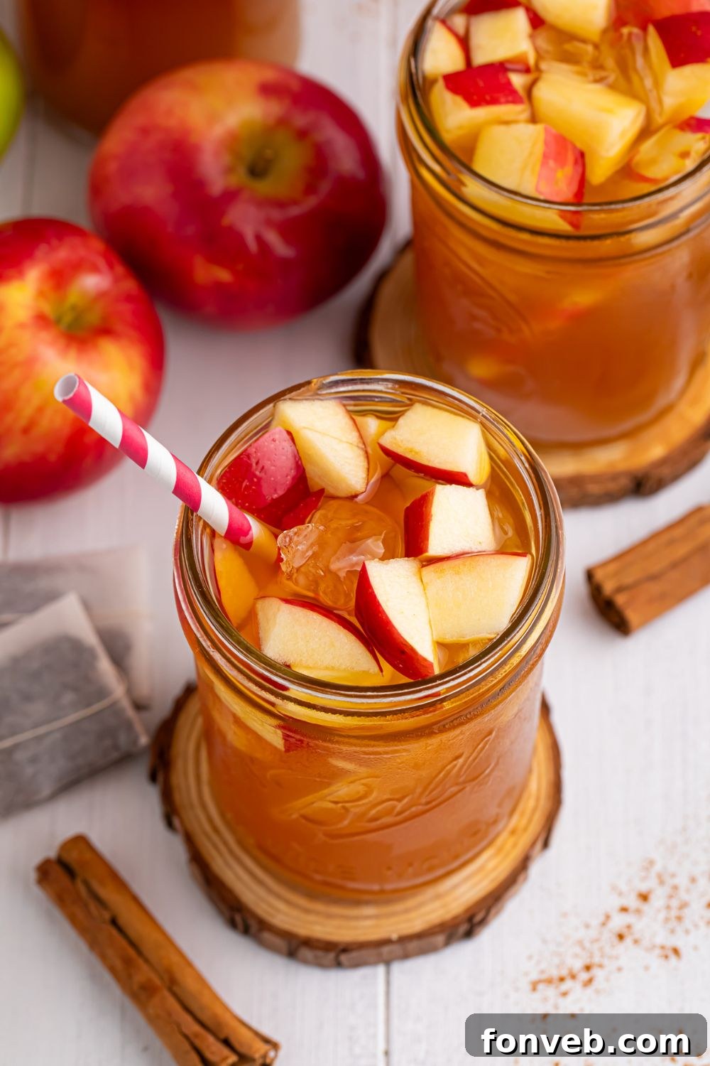 Apple Cider Iced Teas on table in mason jars with apples and cinnamon sticks spread over the table and fresh diced apples in the glasses