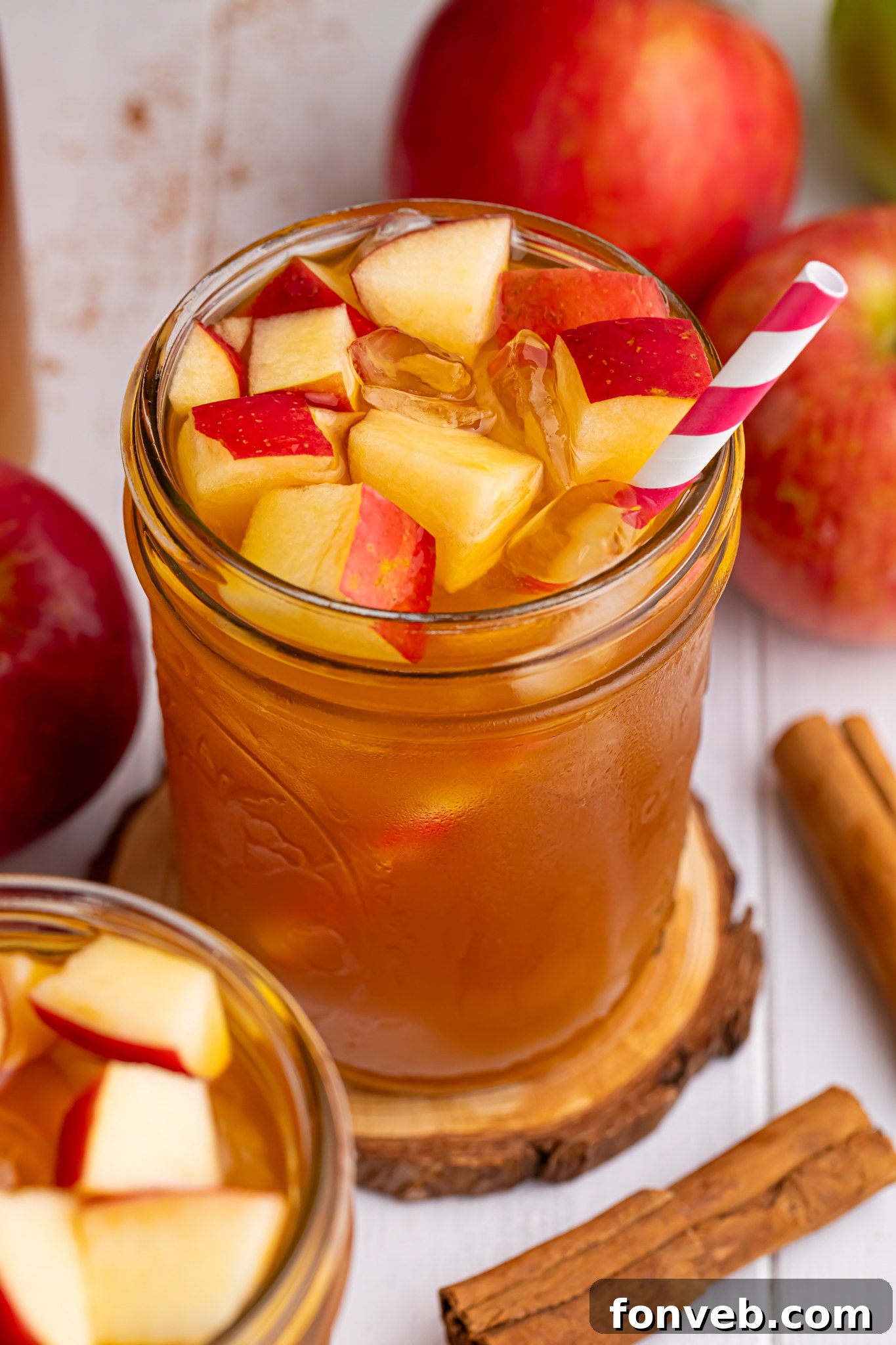 apple cider iced tea in a glass with an overhead look of glass with a straw in it and diced fresh apples with ice cubes