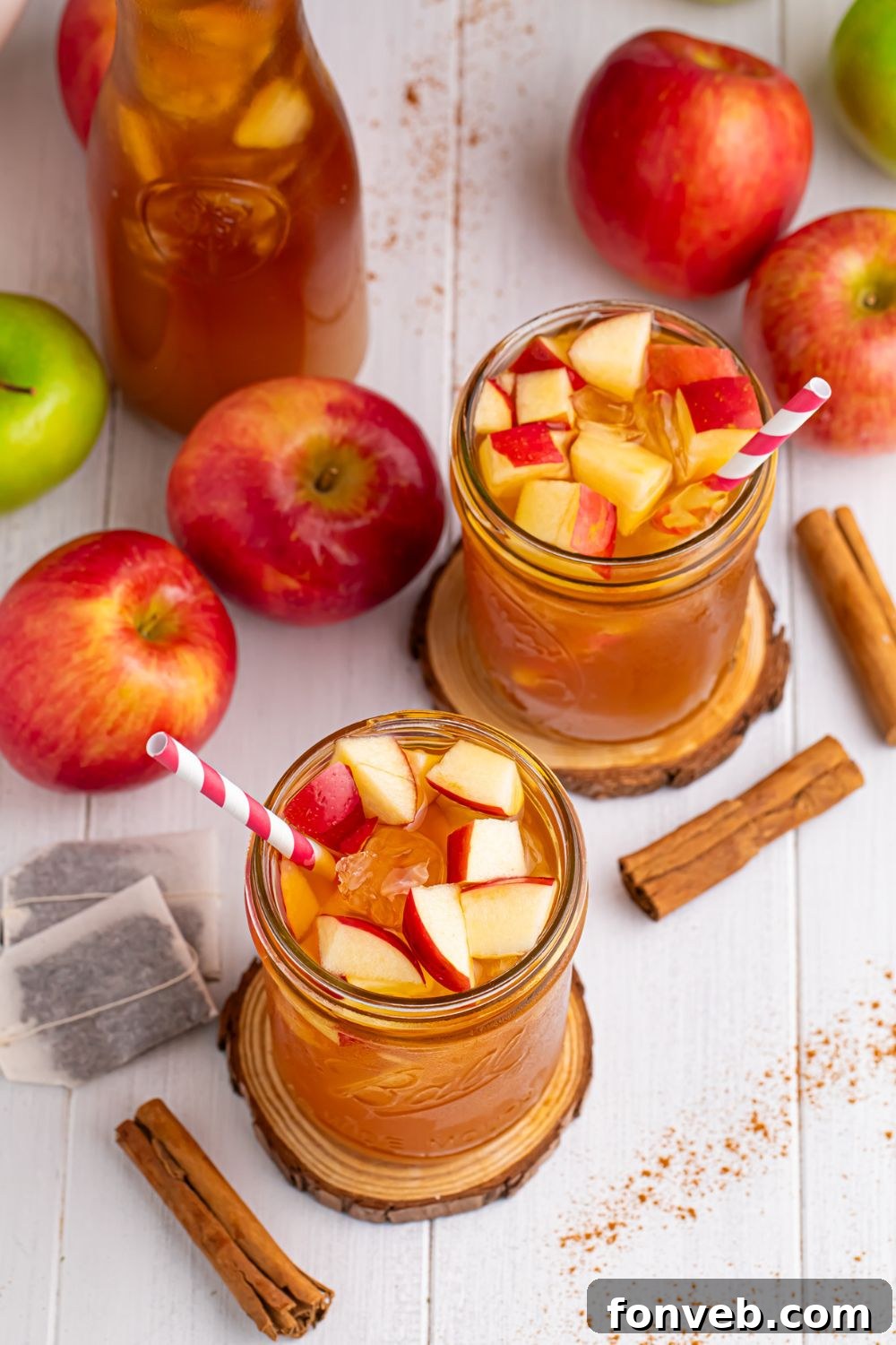 table setting with apple cider teas in glasses with straws. Tea bags, a variety of apples, cinnamon sticks and pitcher of tea all on table 