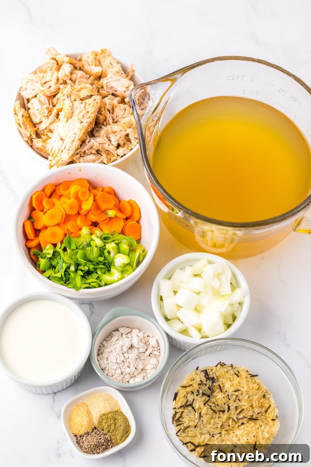 ingredients for this turkey and rice soup all in single bowls on table: stock, vegetables, diced turkey, seasonings, heavy cream, and more. 