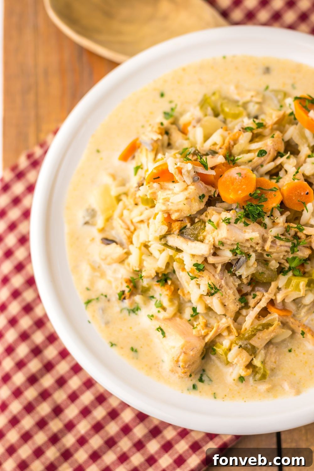bowl of turkey soup on table with a red checked towel under it and wooden spoon to the side