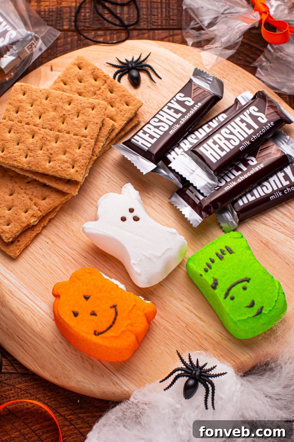 Spooky S'mores Kits 6 Halloween Smores Gift Bag ingredients on a round cutting board with plastic spiders and halloween decor around it