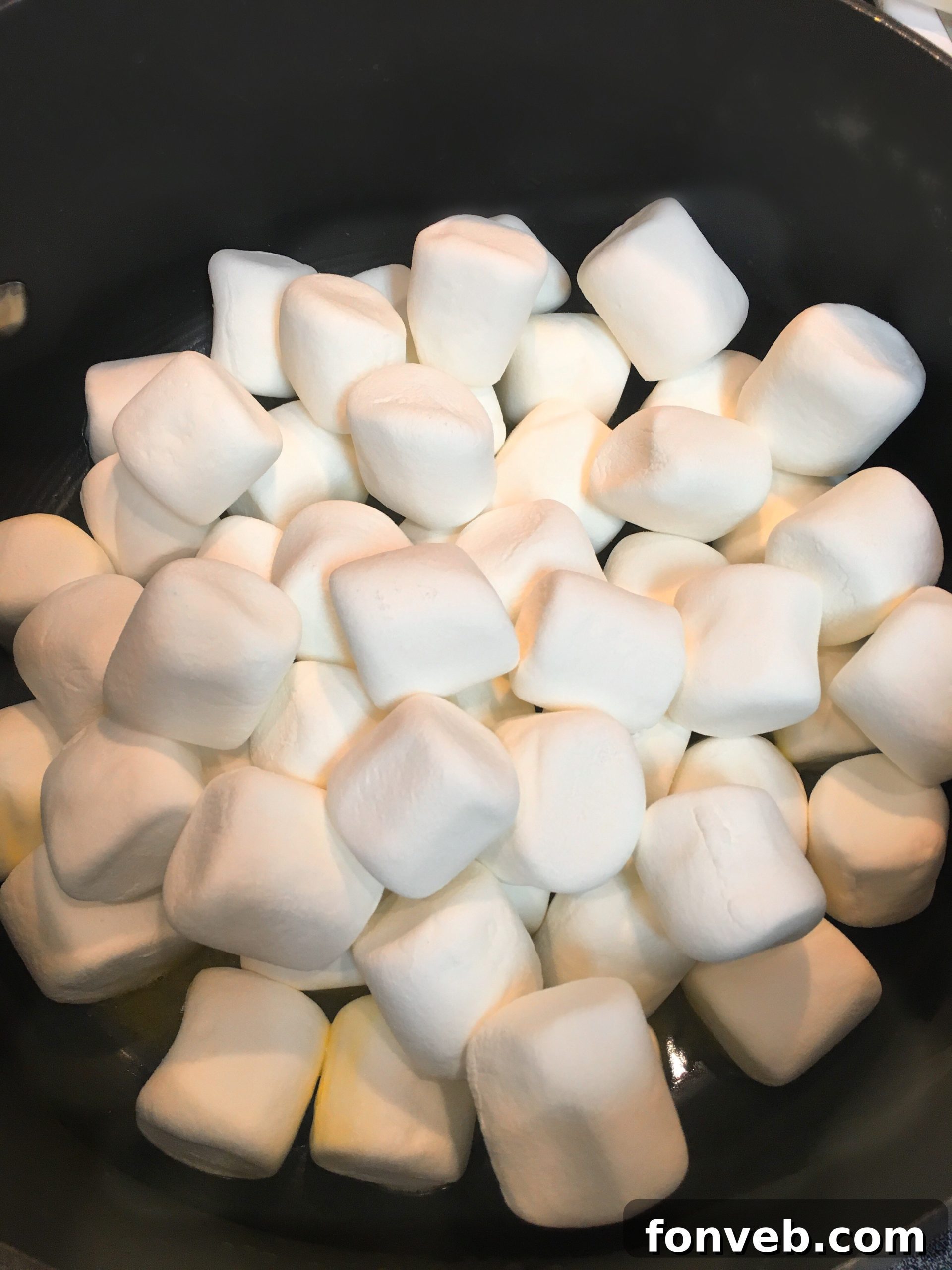 Close-up of a hand gently pressing the Lucky Charms cereal mixture into a greased baking pan.