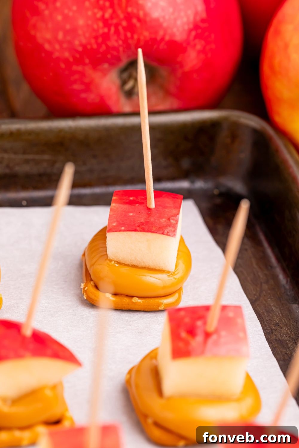 caramel apple treats with toothpicks poking in sitting on a baking tray on table 