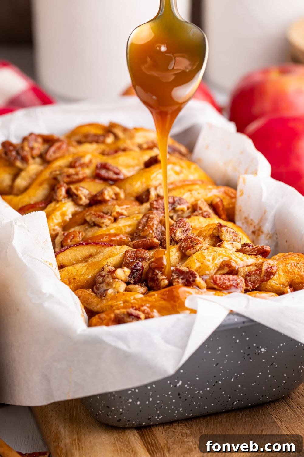 Apple Pie Monkey Bread 14 caramel sauce dripping off a spoon onto the Apple Pie Pull Apart Bread in a pan on the table
