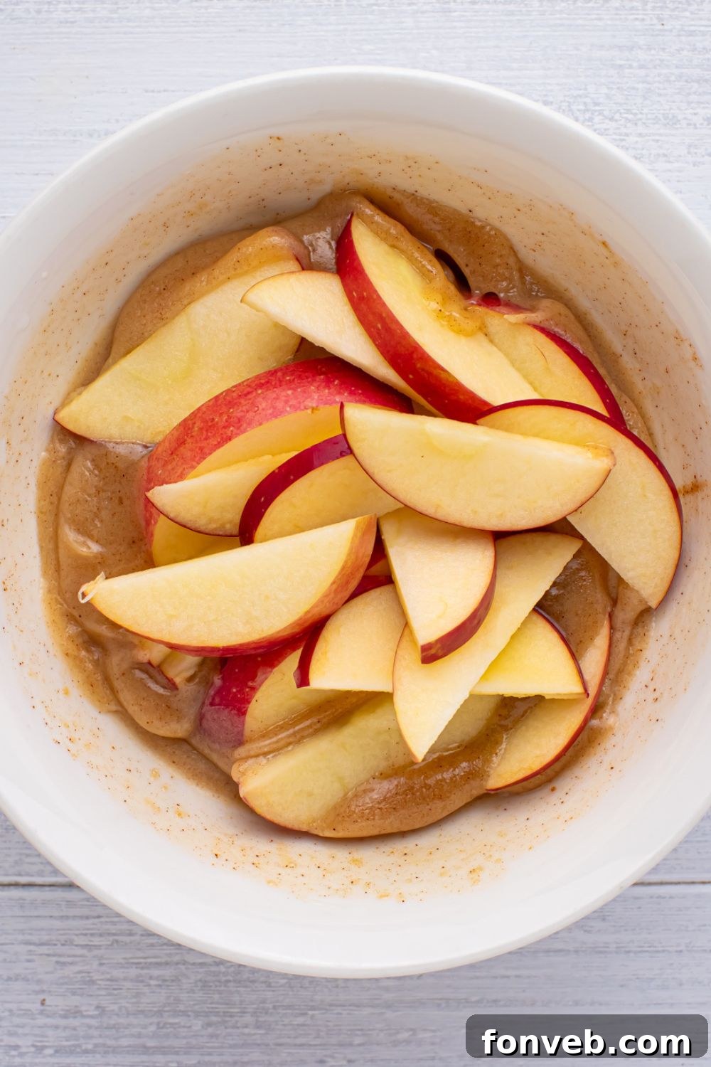 Apple Pie Monkey Bread 7 sliced apples in a butter mixture sitting on table in a white bowl