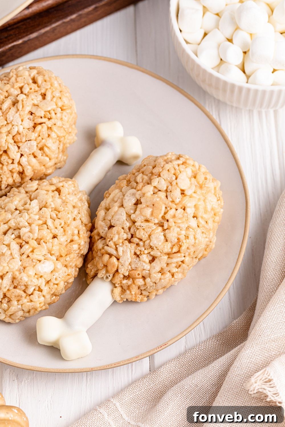 Festive Rice Krispie Drumsticks 17 A delicious Rice Krispie Treat Turkey Leg featured on a white plate, accompanied by a small bowl of mini marshmallows, ready to be enjoyed.